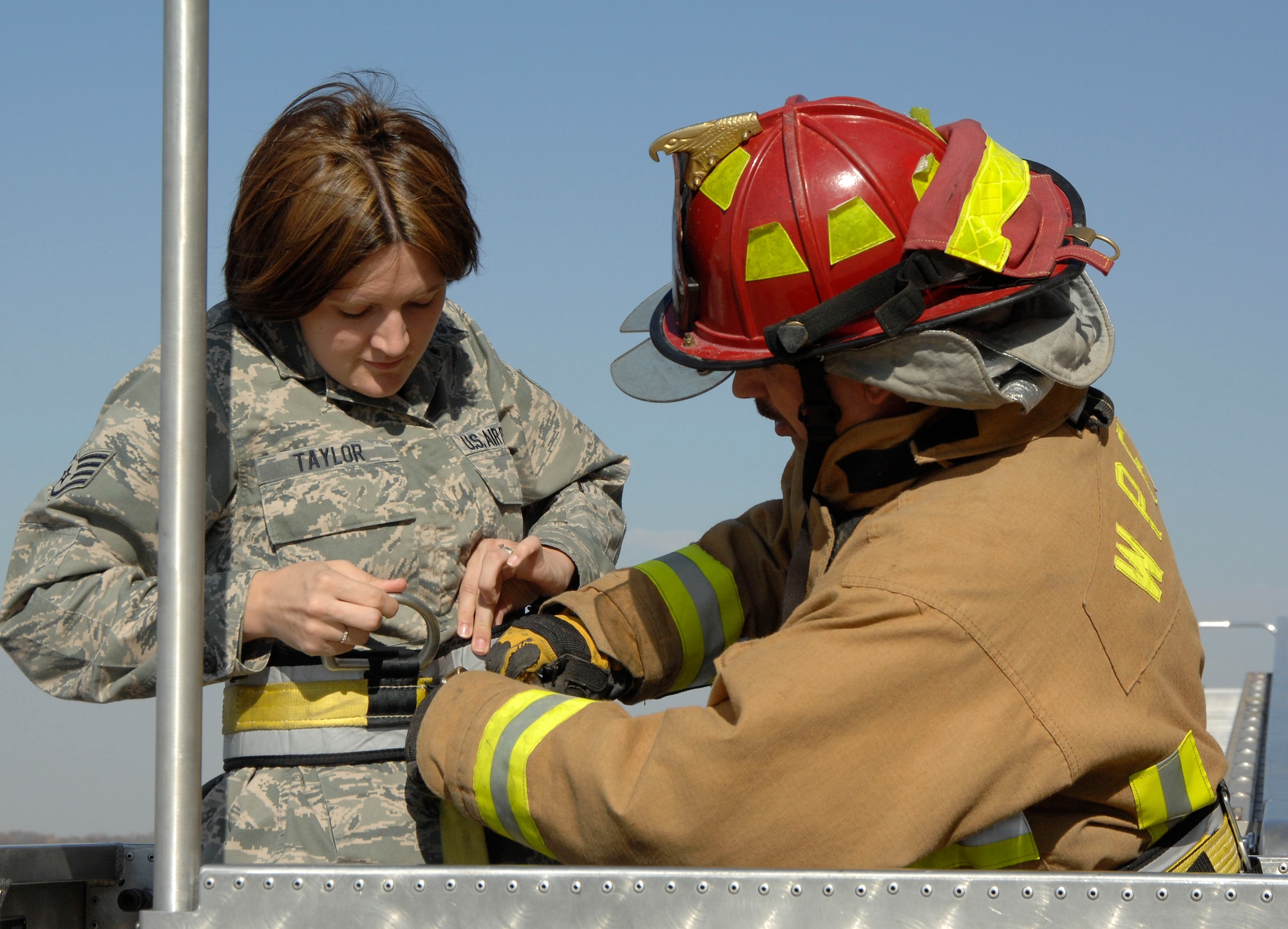 Wright-Patterson Air Force Base firefighter Daryle Phelps assists Staff Sgt. Cassie Taylor, air traffic controller with the 88th Operations Support squadron, in securing a safety harness to the basket of Wright-Patt's 95-foot aerial platform.  The training scenario involved air traffic controllers "trapped" in the tower due to a fire in Building 206 who had to be rescued by the ladder truck. (U.S. Air Force photo/William Pugh)
