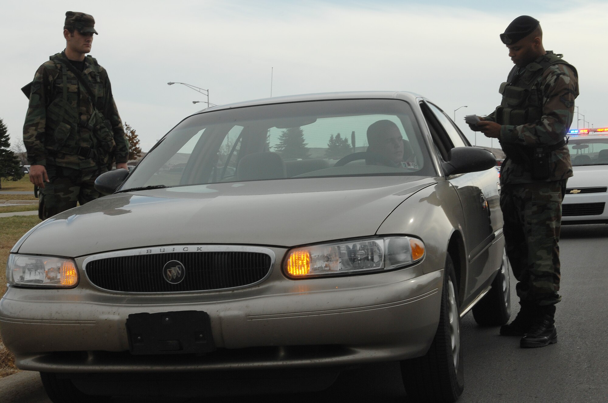 (Right) Airman 1st Class Gerald Rucker, 28th Security Forces base security patrol journeyman, checks the identification, insurance and registration of an Airman, while Airman 1st Class Ryan McCool, 28th Aircraft Maintenance Squadron aerospace maintenance apprentice, performs an over-watch of the vehicle's occupant during a routine traffic stop here, Nov. 4. As an augmentee assigned to the 28 SFS, Airman McCool assists security forces members with different aspects of patrol duties. (U.S. Air Force photo/Airman 1st Class Joshua J. Seybert)