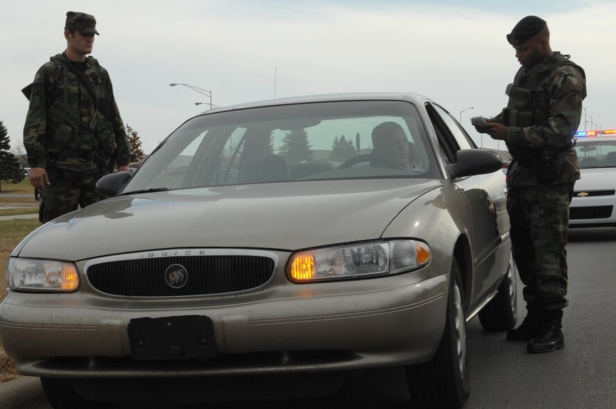 (Right) Airman 1st Class Gerald Rucker, 28th Security Forces base security patrol journeyman, checks the identification, insurance and registration of an Airman, while Airman 1st Class Ryan McCool, 28th Aircraft Maintenance Squadron aerospace maintenance apprentice, performs an over-watch of the vehicle's occupant during a routine traffic stop here, Nov. 4. As an augmentee assigned to the 28 SFS, Airman McCool assists security forces members with different aspects of patrol duties. (U.S. Air Force photo/Airman 1st Class Joshua J. Seybert)