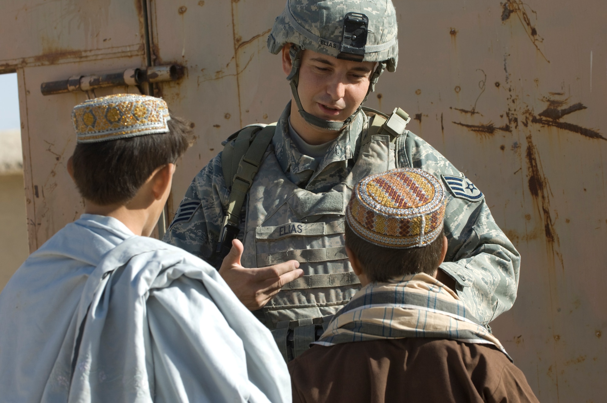 QALAT, Afghanistan -- Air Force Staff Sgt. Don Elias talks with two Afghan boys while providing security during a veterinary outreach held by the Zabul Provincial Reconstruction Team. The team provided free treatment to the nomadic Kuchi tribe's livestock. Sergeant Elias is deployed to the PRT as the force protection NCOIC from Wright-Patterson Air Force Base, Ohio. He is a native of Buffalo, N.Y. (U.S. Air Force photo/Master Sgt. Keith Brown)