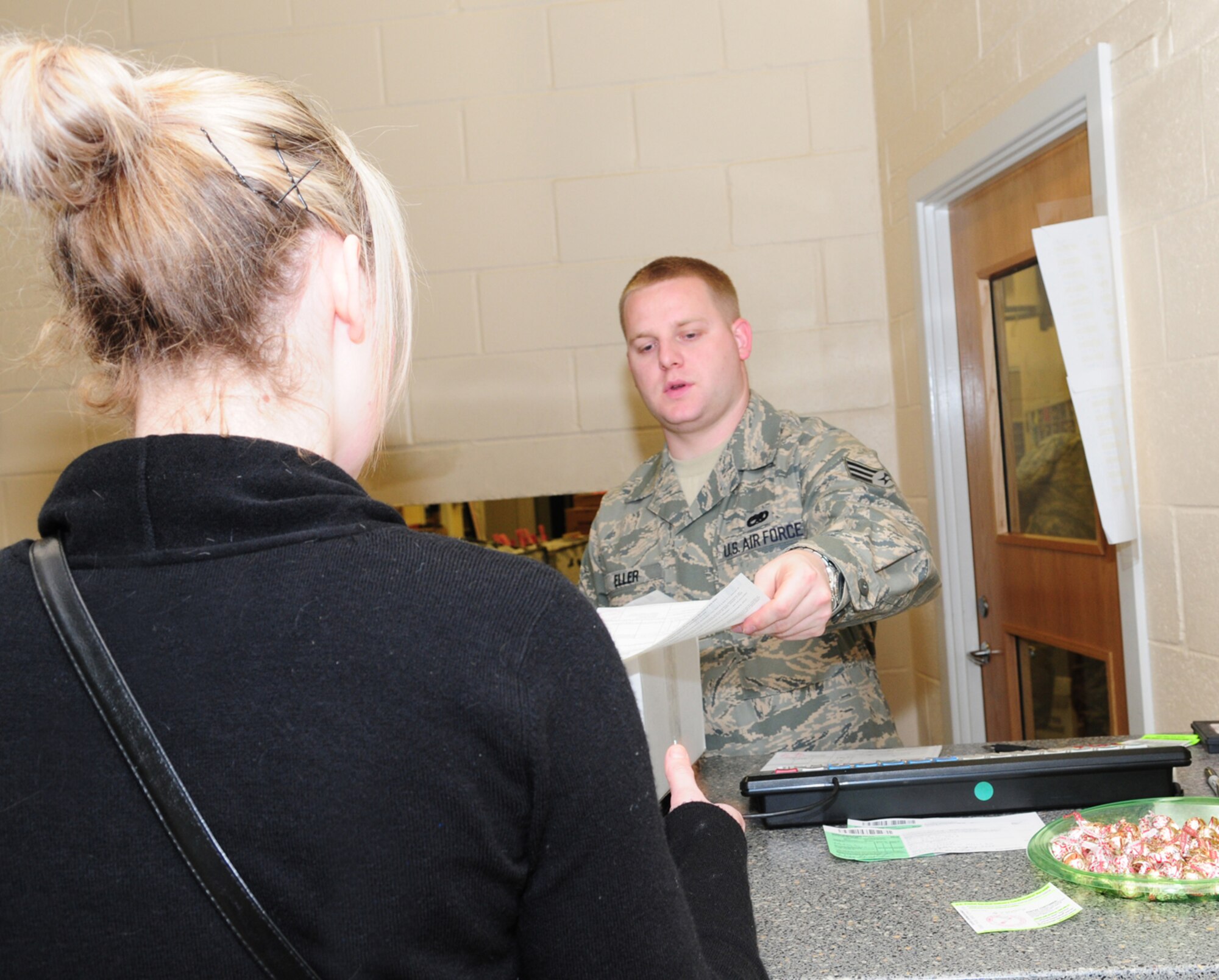 Senior Airman Erik Eller, 100th Communications Squadron Post Office postal clerk, helps a customer mail a package. During the holiday season, the post office will have reduced hours; however, they are helping customers by offering an appointment before normal customer serice hours for anyone mailing five or more packages. This will help reduce waiting times for customers. (U.S. Air Force photo by Karen Abeyasekere)