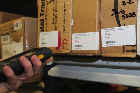 Airman 1st Class Steven Johnson, 100th Communications Squadron Post Office postal clerk, scans the barcode from an incoming package Nov. 4. Once the barcode is scanned, Airman Johnson checks to ensure it is the same number as printed on the label, then checks the last name of the mail box owner, to ensure the package is labelled correctly for the right box. At this time of year, an average of 200 to 300 boxes per day come into the post office, vastly increasing nearer the holidays. Airman Johnson said it usually takes him between 20 to 30 minutes to scan all the packages each day. Once the barcodes are scanned, the information is downloaded to the computer and slips printed out for customers to notify them of their packages. (U.S. Air Force photo by Karen Abeyasekere)