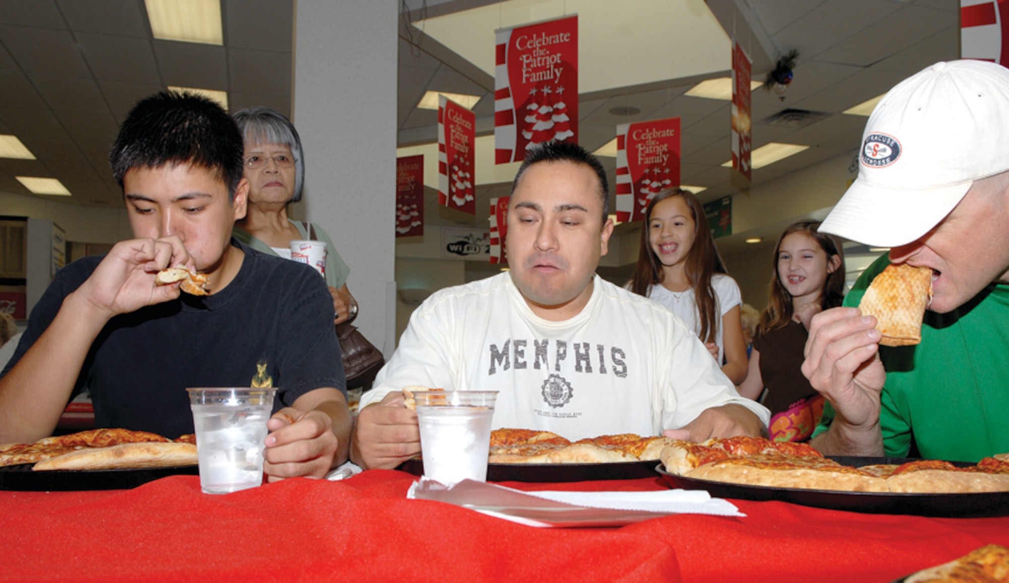 Gabriel Ruiz; his father, Chief Hector Ruiz, North Island Naval Air Station, San Diego, and Tech. Sgt. Douglas McGraw, 56th Equipment Maintenance Squadron Aircraft Structural Maintenance, race to eat as many slices of pizza as possible during Anthony's Pizza Eating Contest held at the food court during the grand re-opening of the Luke Air Force Base Exchange. (U.S. Air Force photo/ Airman 1st Class Ronifel Yasay.)