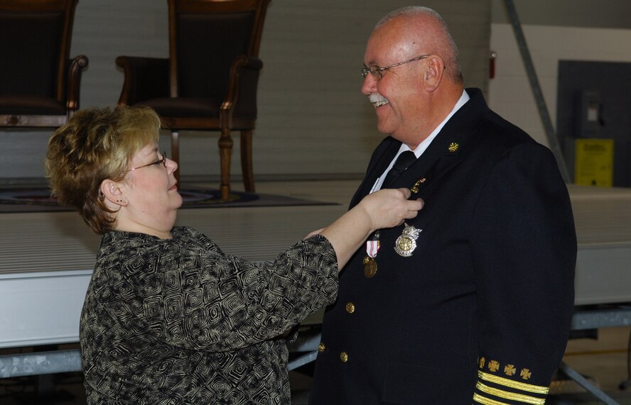 MINOT AIR FORCE BASE, N.D. -- Janet Clifford places a retirement pin on the jacket of husband Fire Chief James D. Clifford during his retirement ceremony here Oct. 31. Chief Clifford was selected as base fire inspector in March 1986, promoted to Assistant Chief of Fire Prevention in 1992 and selected as Fire Chief in July 2001. Chief Clifford has dedicated 33 years of his life toward faithful service to his country and community. (U.S. Air Force photo by Senior Airman Cassandra Jones)
