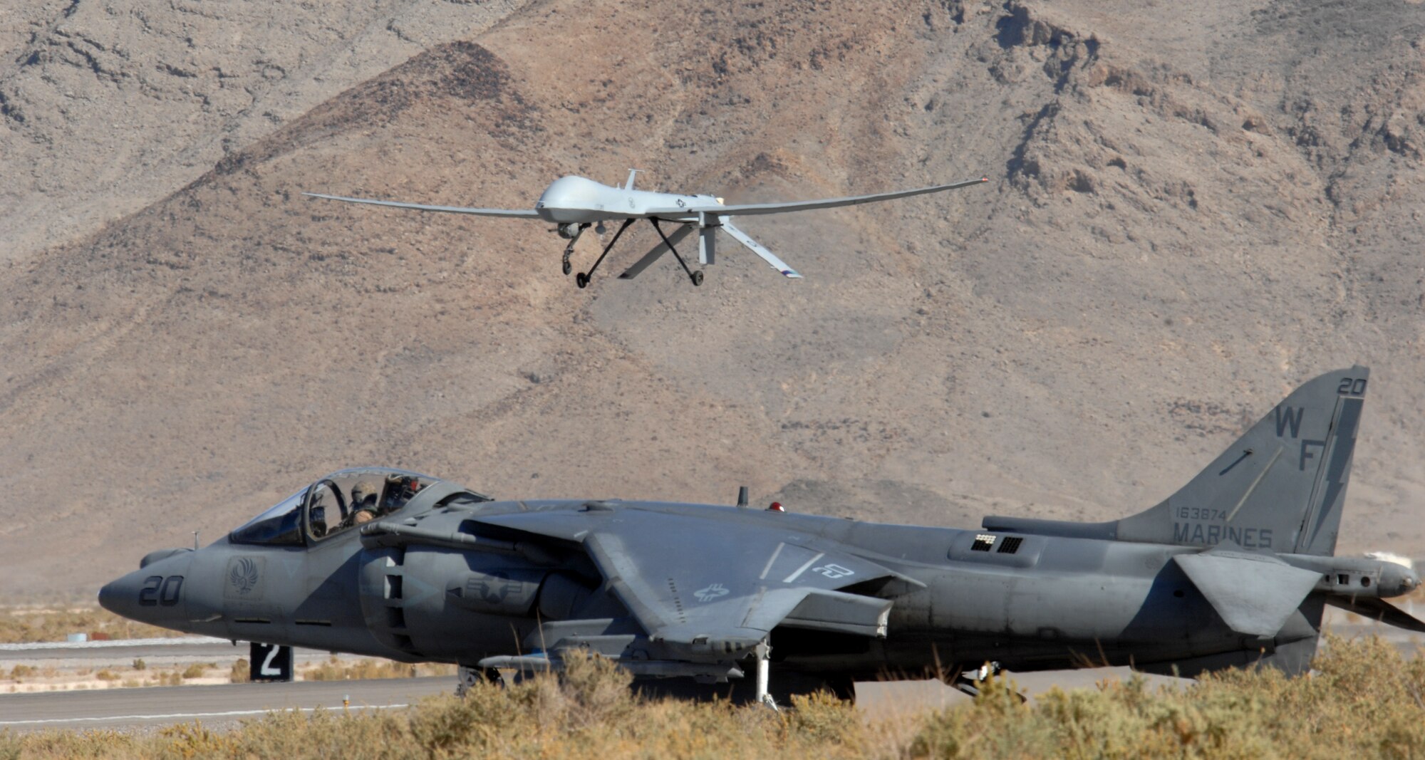 CREECH AFB, Nev. -- A U.S. Marine Corps AV-8B Harrier assigned to Marine Attack Squadron 513, Marine Corps Air Station Yuma, Ariz., waits as a MQ-1 Predator passes by at Creech Air Force Base, Nev.  Members of the 11th Reconnaissance Squadron here teamed up with Marines for a joint training exercise at Creech AFB Oct. 24 to Nov. 7.  (U.S. Air Force Photo/Senior Airman Larry E. Reid Jr.)  