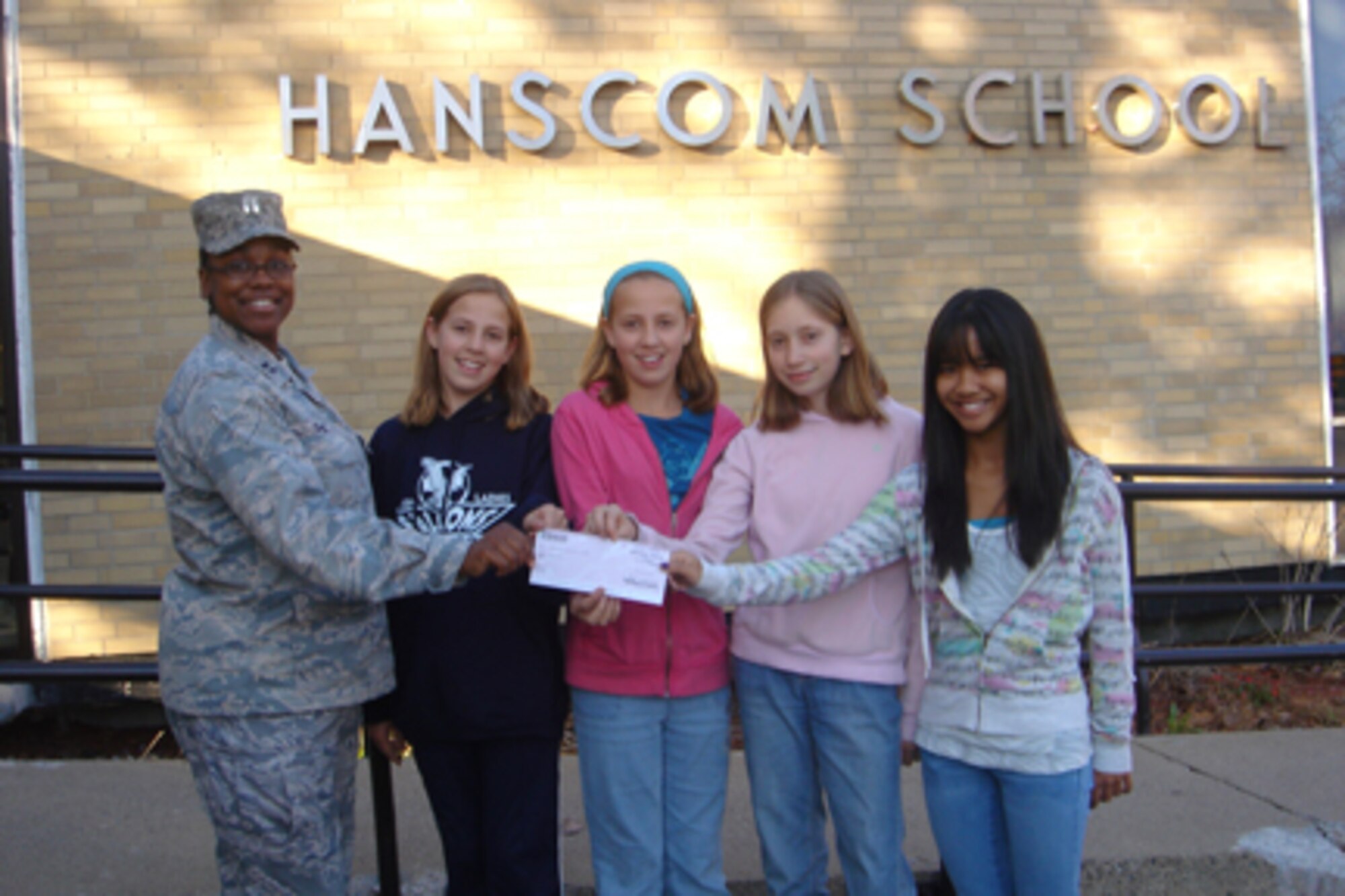 HANSCOM AIR FORCE BASE, Mass. - Hanscom Middle School students donate their recent Hopa Race bake sale proceeds to the Hanscom Troop Care Package Drive. The funds will be used to directly support the base's deployed warfighters. Pictured here Hanscom Company Grade Officer Club representative Capt. Jaquelynn Coles accepts a check from Hanscom Middle School 7th grade students from left to right, Rebekah Boyd, Rachel Boyd, Rebecca Huff, and Sidney Pandes.   