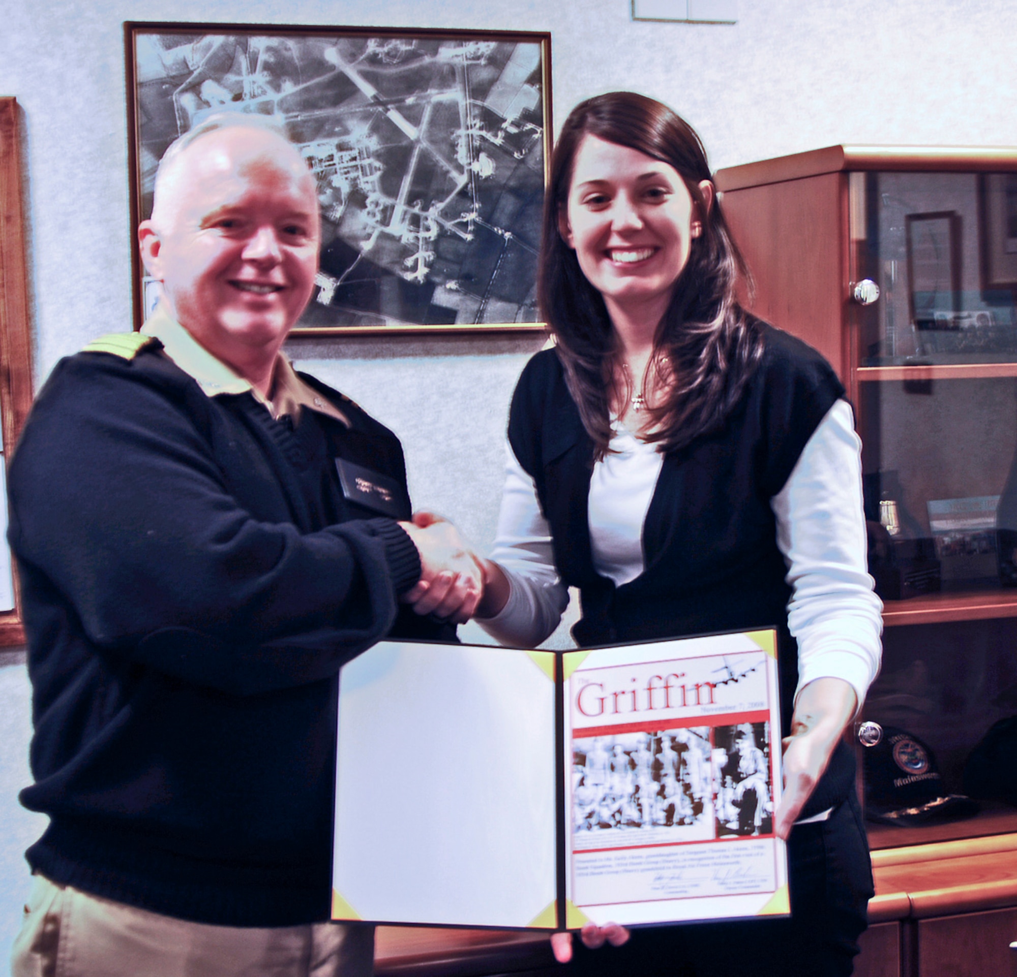 U.S. Navy Captain Henry J. "Harry" Babin presents a certificate to Ms. Kelly Akens commemorating the first visit to the base by a grandchild of the 303rd Bomb Group.  Ms. Akens honored her grandfather Sergeant Thomas I. Akens who flew 6 missions over Nazi occupied Europe during the Spring of 1945 as the war in Europe drew to a close. (U.S. Air Force Photo by Staff Sgt. Janaine Paige)