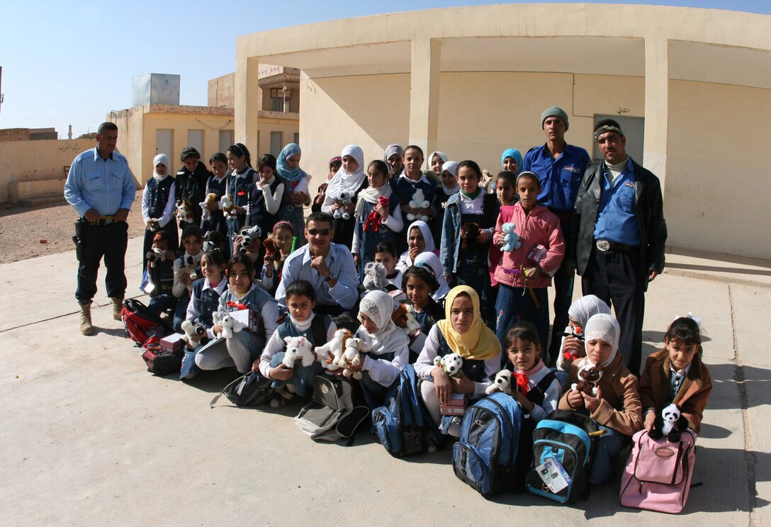 Iraqi police from Rutbah, Iraq, share a photo opportunity with students from Intifathatil Aqsah Primary School following a distribution of backpacks and school supplies Nov. 11.  Along with Coalition forces, the police officers handed out an array of items, many purchased and sent to Iraq by patriotic citizens from throughout the United States.::r::::n::