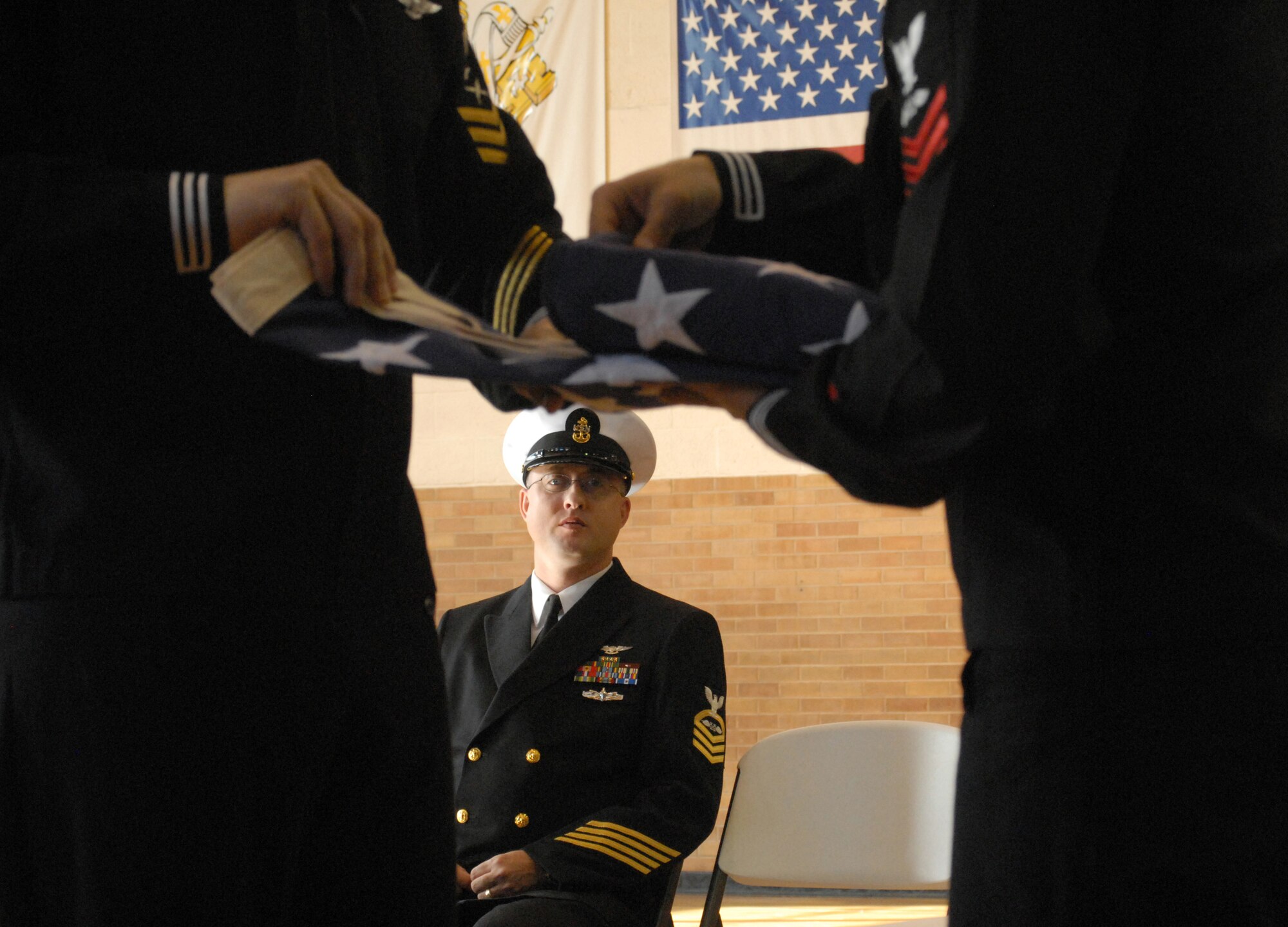 Chief Petty Officer Henry Cooper, Fire Academy Navy Chief Liaison, Goodfellow AFB, Texas, looks on as Petty Officer First Class David Norman and First Class Petty Officer Steven Vlasich both from the Center for Information Dominance Navy Detachment, Goodfellow AFB, Texas folded the U.S. flag and presented it to the Angelo Catholic School, San Angelo, Texas, at a Veterans' Day Ceremony on Nov. 11. The sailors conducted the flag ceremony and flew the flag for the school of approximately 80 students. (U.S. Air Force photo by Senior Master Sgt. Robert Martinez)