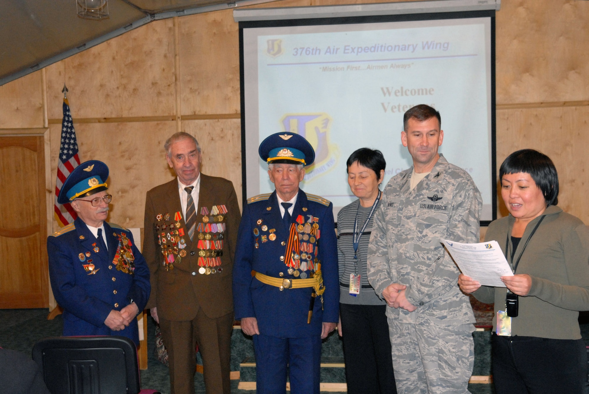 Aigul Karymshakova reads a poem prepared by retired Soviet air force Col. Vasili Strelnikov (center), to Manas Airmen during a Veterans Appreciation Day visit by ten Kyrgyz World War II veterans, Nov. 11. Listening from left to right are retired colonels Yuri Krupin, Nikolai Nikiforov and Strelnikov, interpreter Valentina Turabekova, and Col. Christopher Bence, 376th Air Expeditionary Wing commander. Ms. Karymshakova is an Manas AB media outreach specialist. (U.S. Air Force photo/Senior Airman Ruth Holcomb)