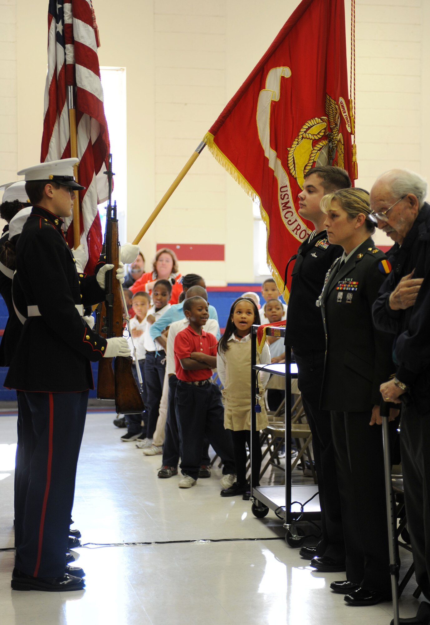 LANGLEY AIR FORCE BASE, Va.-- Four members of the Marine Corps Junior Reserve Officer Training Corps at Phoebus High School present the colors while elementary school children sing and servicemembers look on during "Take a Veteran to School Day" at Jane H. Bryan Elementary School Nov. 11. The event gave Hampton school children a chance to meet and honor local servicemembers and veterans. (U.S. Air Force photo/Airman Rebecca Montez)