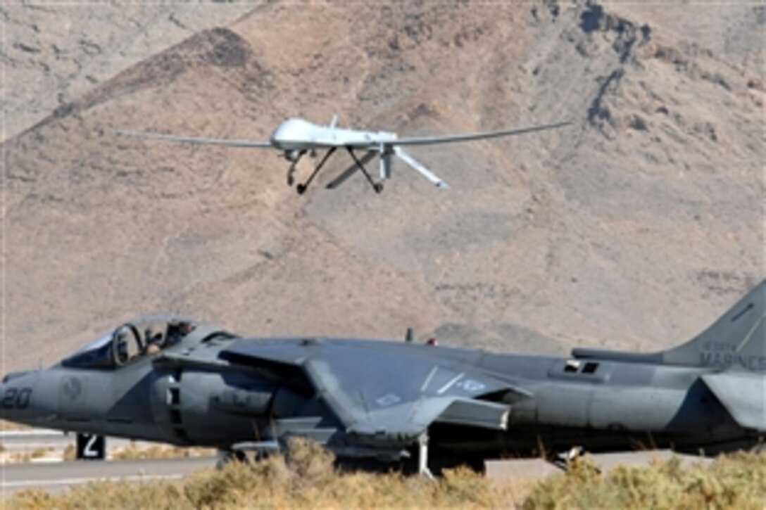 A U.S. Marine Corps AV-8B Harrier aircraft waits for takeoff as an MQ-1 Predator unmanned aerial vehicle passes overhead on Creech Air Force Base, Nev., Nov. 4, 2008. The airmen, assigned to the 11th Reconnaissance Squadron, have teamed with Marines for a joint training exercise on the base.