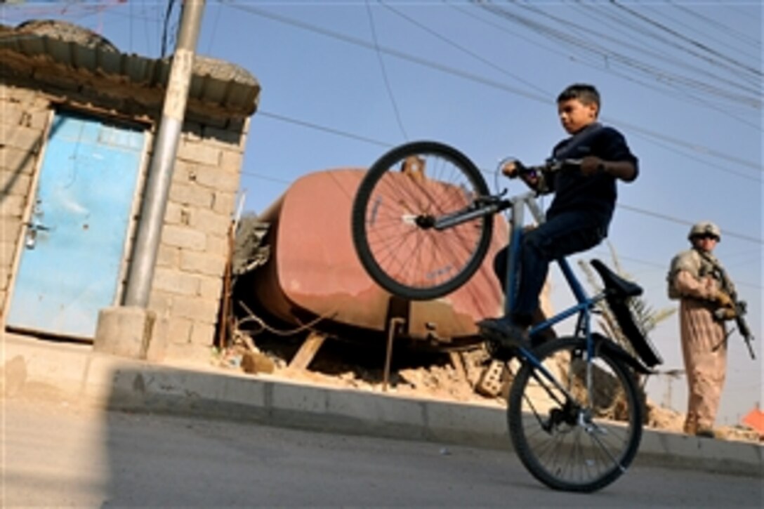 A U.S. Air Force airman, accompanying Iraqi police officers, watches an Iraqi boy "pop a wheelie" while on patrol in the Al Bayaa community of southern Baghdad, Iraq, Nov. 7, 2008. The airmen are assigned to Detachment 3, 732nd Expeditionary Security Forces Squadron, 1st Brigade Combat Team, 4th Infantry Division.
