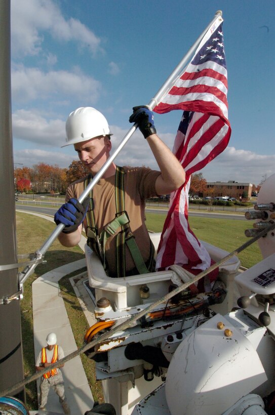 Poised approximately thirty-feet high inside a bucket truck, Airman 1st Class David Posey, 316th Civil Engineer Squadron electrical systems apprentice, positions a United States flag inside a flag pole holder on Alabama Avenue Nov. 7, prior to Veterans Day.(U.S. Air Force photo by Bobby Jones)
