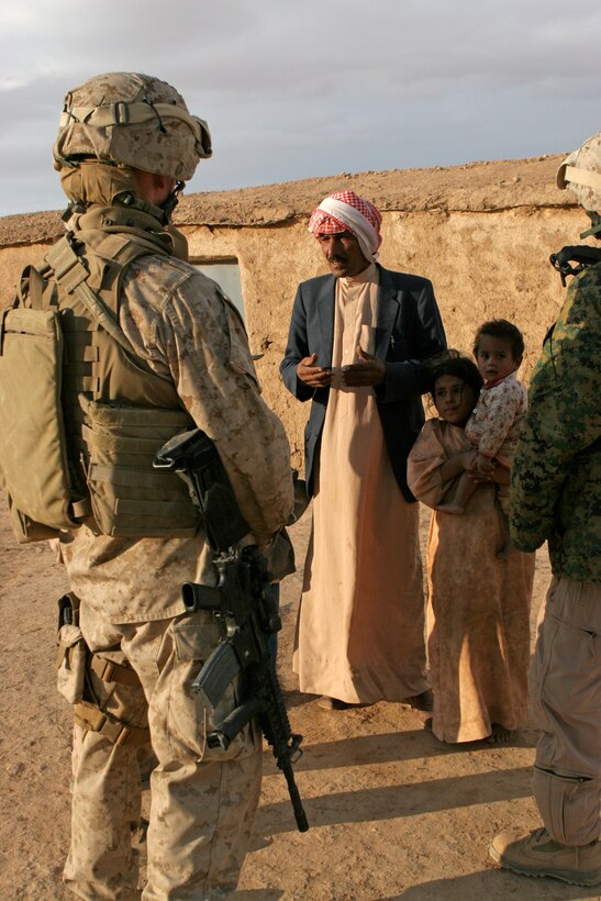 Lt. Col. Andrew J. Drake, plans officer, Jump command point, Multi National Force - West, and Danny, an interpreter, speak to an Iraqi man and his family in the countryside outside Al-Ba'aj, during a visit to promote good relationships and security for the Marines and Iraqis.