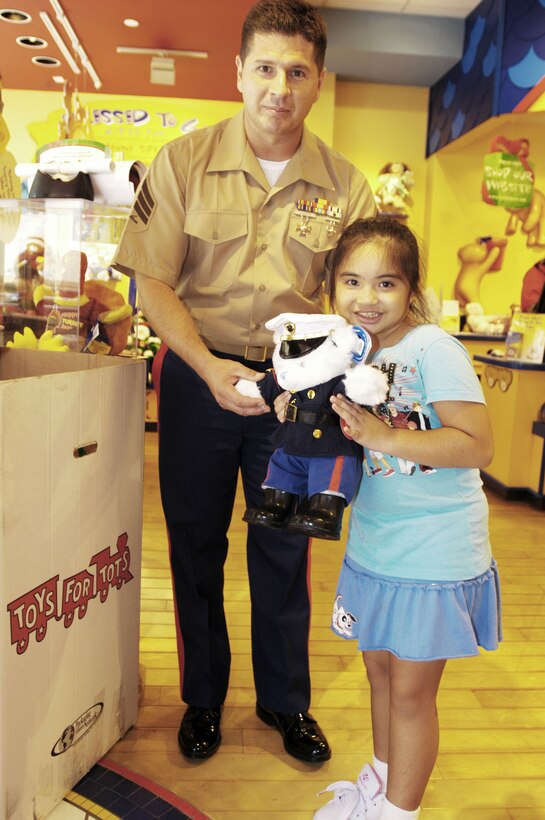 Pakalana Shiraki, 7, of Honolulu hands a bear she built to Sgt. Jose Godinez, 4th Force Reconnaissance Company, at the Ala Moana Build-a-Bear Workshop Nov. 15. Marines were on hand accepting donations to the Marine Corps Reserve's annual Toys for Tots campaign.