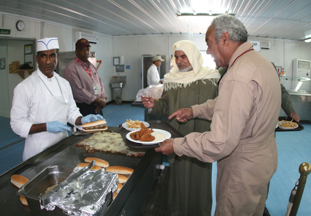 Assisted by Khamis Ahmed Ali-Mussbeh (right), an Arabic interpreter with 2nd Battalion, 25th Marine Regiment, Regimental Combat Team 5, Iraqi imam Mahmoud Ahmed Nudin Obid (center), a religious leader in western al-Anbar province, browses the serving line at the Camp Korean Village dining facility following a base religious service Nov. 16.  The imam addressed the U.S. troops during the service, encouraging them to study about our religion while they are here.  ::r::::n::