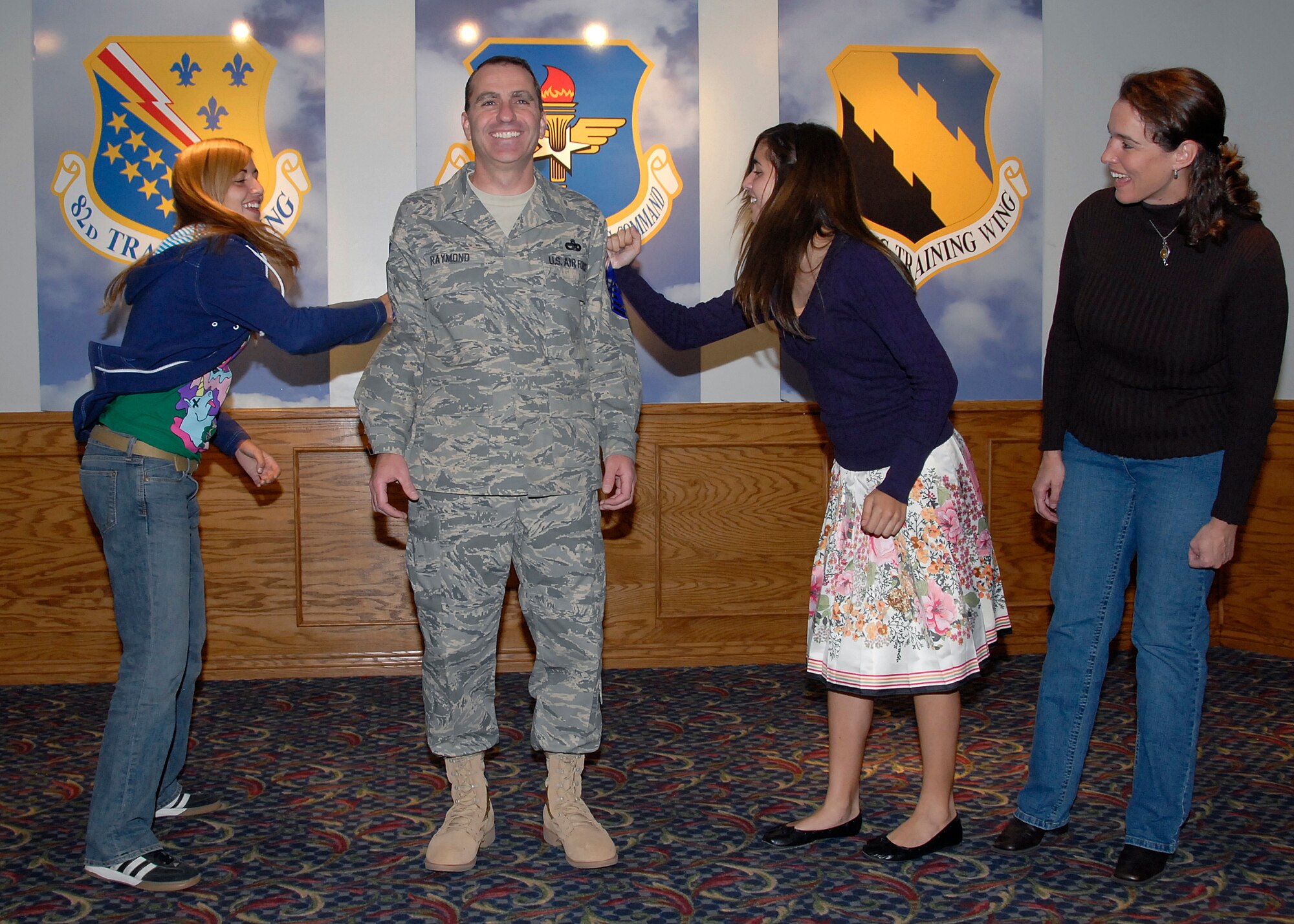 Julia Raymond, left, and her sister, Kelly, tack on chief master sergeant stripes to their father's sleeves Nov. 14 during a promotion party at the Sheppard Club. Senior Master Sgt. Paul Raymond, center, was among four Sheppard sergeants selected for promotion to E-9. Also pictured is Susan, Sergeant Raymond's wife. (U.S. Air Force photo/Mike Litteken)