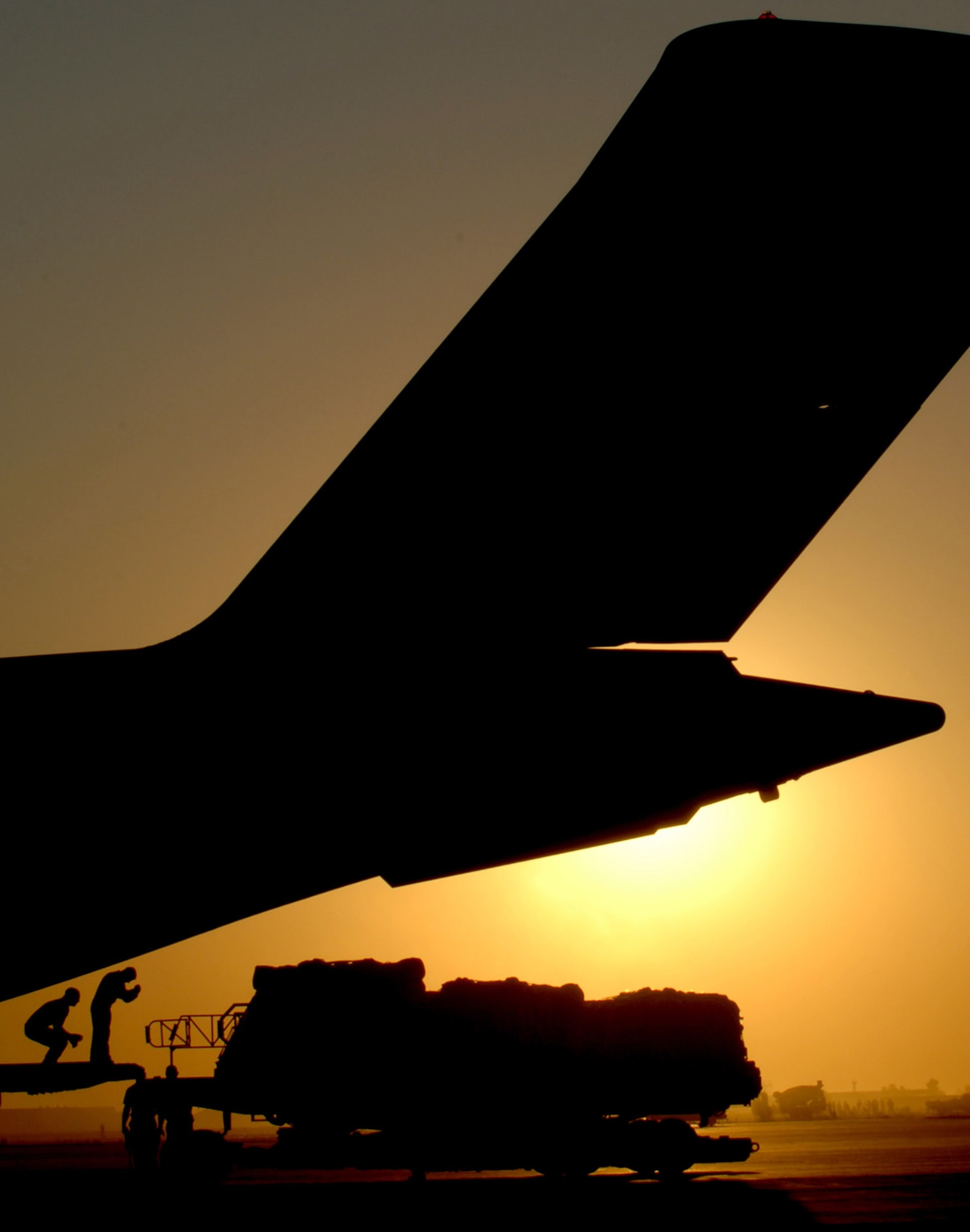 The sun sets behind a C-17 Globemaster III as Airmen guide a K-loader into position Nov. 17 at Joint Base Balad, Iraq. Airmen at the aerial port at Joint Base Balad move more cargo per year than Dover Air Force Base, Del.; Charleston AFB, S.C.; and Travis AFB, Calif., combined. The C-17 is deployed from the 437th Airlift Wing at Charleston Air Force Base, S.C. (U.S. Air Force photo/Tech. Sgt. Erik Gudmundson) 
