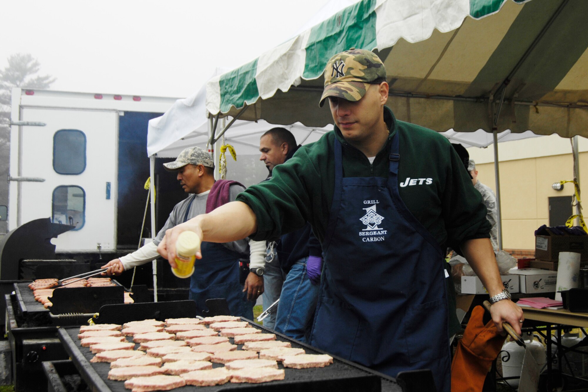 HANSCOM AIR FORCE BASE, Mass. – Volunteers (from left to right) Senior Master Sgt. Raul Ruiz, Senior Master Sgt. Ken Theriault, and Master Sgt. John Carbon grill burgers and hot dogs in the rain prior to the start of the Unit Compliance Inspection celebration at the Tennis Bubble Nov. 14. During the event, Brig. Gen. Terry Feehan, Electronic Systems Center vice commander offered remarks, presented certificates and congratulated ESC personnel on their performance. (U.S. Air Force photo by Linda LaBonte Britt)