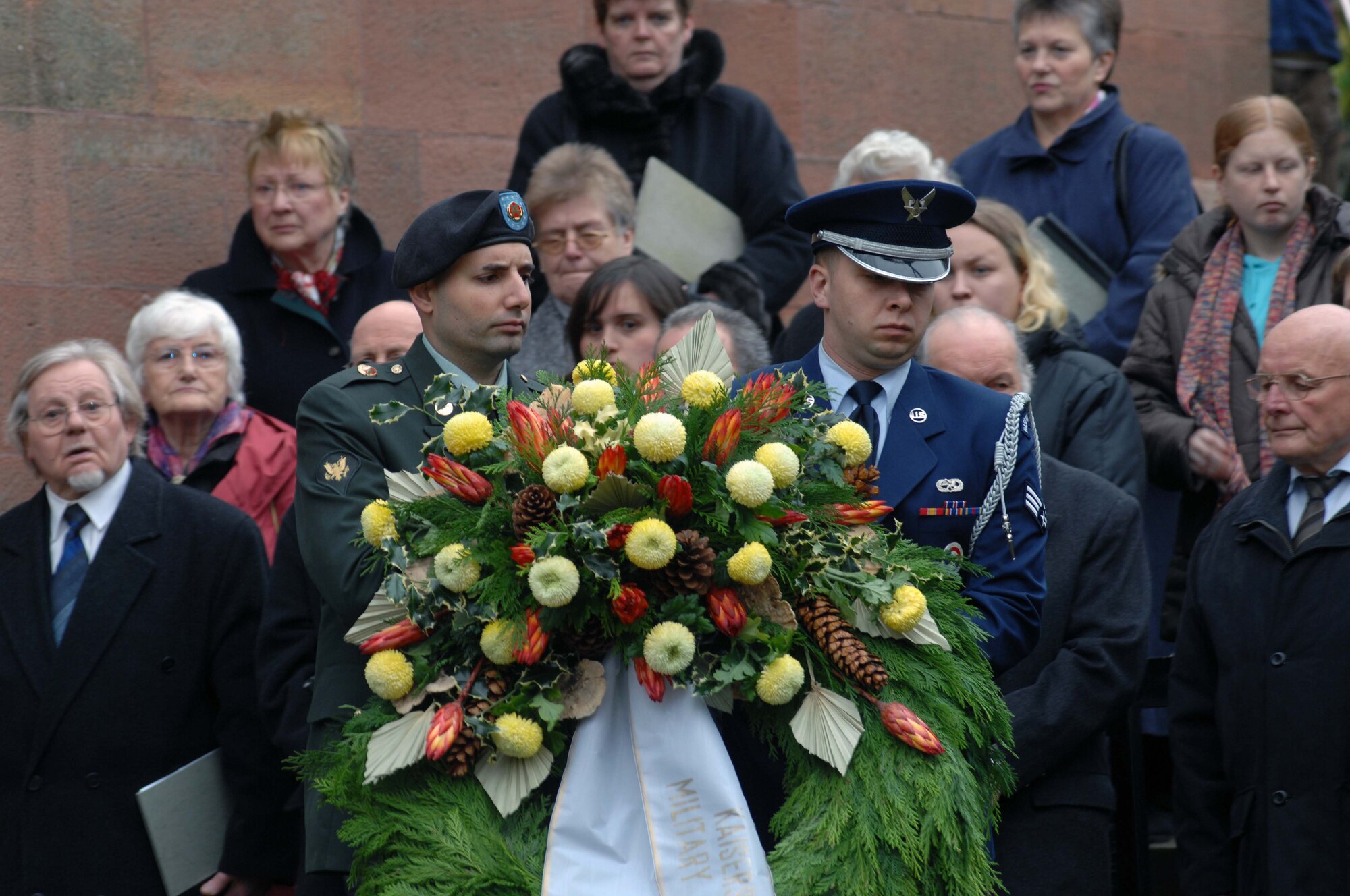Spc. Vincent Holtzman, from the U.S. Army Garrison Kaiserslautern's Directorate of Human Resources and Senior Airman Brian Lapiska, from the 86th Airlift Wing’s 1st Combat Communications Squadron present the Kaiserslautern military community's wreath during the German National Day of Mourning ceremony Sunday at the Soldiers' Monument in the Kaiserslautern Cemetery. More than 150 people from several different nationalities attended the ceremony. The National Day of Mourning or Volkstrauertag is a public holiday in Germany that is observed two Sundays before the first Advent - the Sunday that is in the period from Nov. 13 to 19. This German holiday is similar to the United States' "Veteran's Day," except that it commemorates all victims who died during wars. It was first observed in Germany in 1952. The city of Kaiserslautern and the German Association of War Graves have held the Volkstrauertag wreath-laying ceremony at the Soldiers’ Monument in the Kaiserslautern Cemetery for 25 years. The ceremony usually consists of about 10 wreath presentations, one of which is from the Kaiserslautern military community where an Airman and Soldier will present the wreath and alongside an Air Force and Army officers will render a salute. The U.S. Army Garrison Kaiserslautern has participated in this ceremony since it was established in 1992. With two eternal flames, the Soldiers’ Monument watches over military graves from World War I and World War II. U.S. Army photo by Christine June, USAG Kaiserslautern.