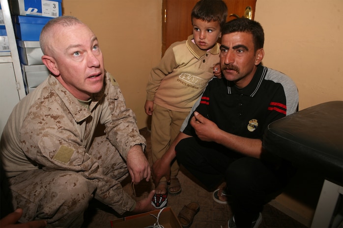 Lt. Cmdr. Michael Tomlinson, a Navy chaplain with Task Force 1st Battalion, 2nd Marine Regiment, Regimental Combat Team 1, helps a young Iraqi boy and his father try on the child's new shoes, Nov. 18 in Saqlawaiyah, Iraq. During one of the last operations before the battalion departed the area, about 500 pairs of childrenâ??s shoes were donated to Iraqi families as part of the ongoing "Operation Happy Feet," headed by Tomlinson.   The battalion is now part of Regimental Combat Team 5 and will be operating out of Rawah.