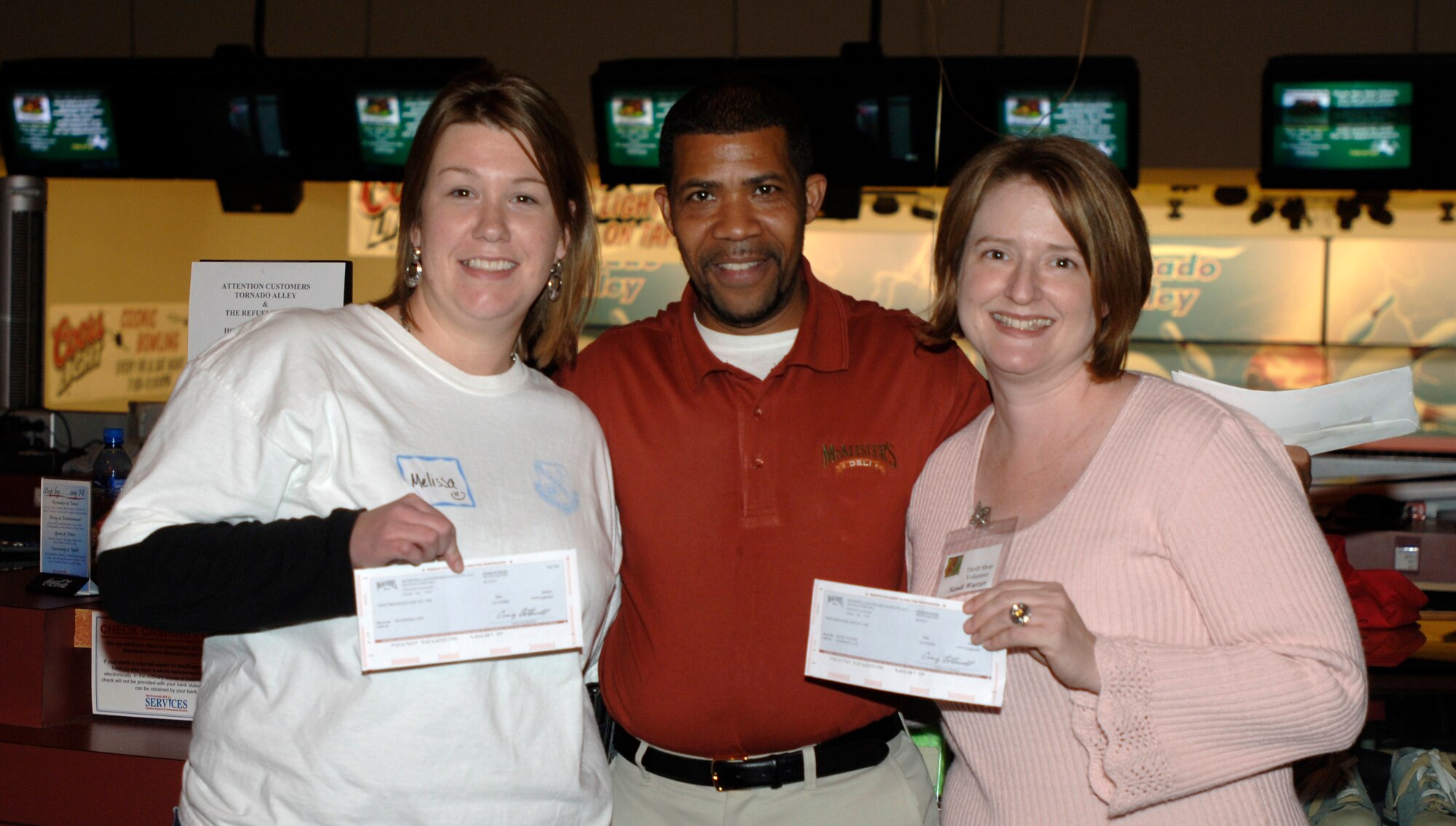 MCCONNELL AIR FORCE BASE, Kan. -- Melissa Flint, McConnell Enlisted Spouse’s Club president, and Sandi Wurzer, McConnell Officer Spouse’s Club president, receive donation checks worth $1000 each from Robert Patton, McAlister’s Deli’s general manager, at the McConnell Air Force Base bowling alley, Nov. 17. The organization continued their bowling event with a cake-cutting ceremony. The club’s newly coined phrase, “individually we contribute; together we make a difference,” was iced across the top. (Photo by Senior Airman Laura Suttles)