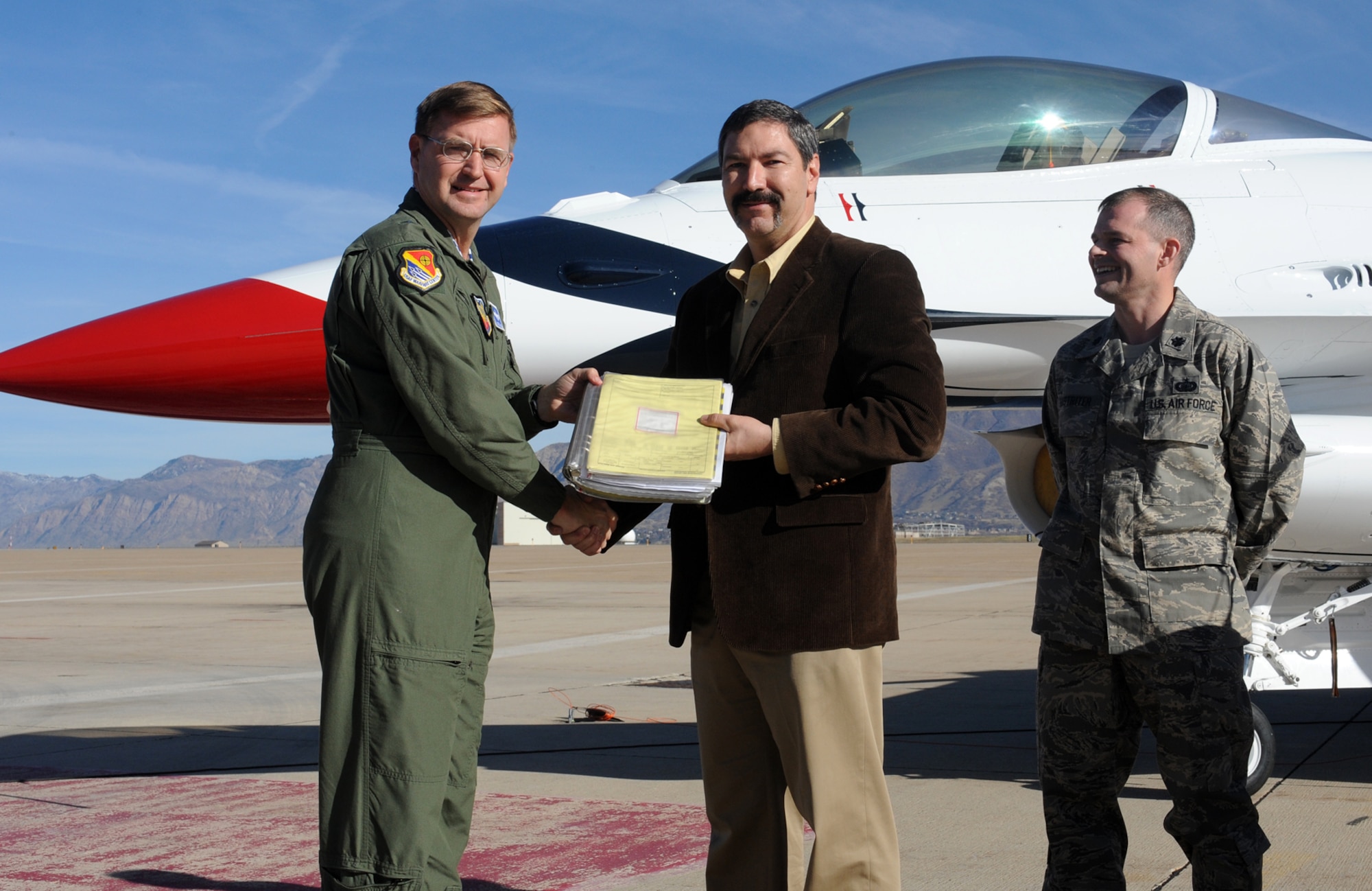 Lt. Col. Michael Hastriter, 501st Aircraft Sustainment Squadron commander (right), watches as Brig. Gen. Stephen Hoog, U.S. Air Force Warfare Center commander (left), receives an F-16 log book from Greg Hoffman, 573rd Maintenance Squadron Director (center), symbolizing the official handing over of the last Block 52 F-16C for the U.S Air Force Thunderbirds Aerial Demonstration Team during a ceremony November 17 at Hill Air Force Base, Utah. (U.S Air Force Photo by Alex Lloyd)