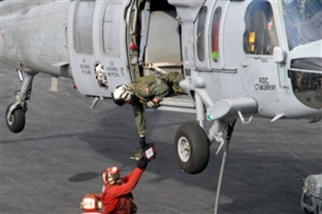 An aircrewman assigned to the "Blackjacks" of Helicopter Combat Support Squadron 21 leans out of an MH-60S Sea Hawk as it hovers above the flight deck of the Nimitz-class carrier USS Ronald Reagan to hand a container to flight deck personnel, Pacific Ocean, Nov. 14, 2008. The USS Ronald Reagan is on a routine deployment, currently operating in the U.S. 7th Fleet area of responsibility.