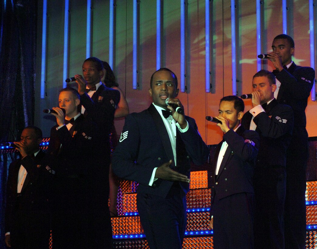 Staff Sgt. Corey Sims is accompanied by the Tops in Blue troupe while singing 'God Bless the U.S.A,' to a capacity crowd at the Andrews Reel Time Theater Nov. 14. The song, by country singer Lee Greenwood, has become a closing anthem for Tops in Blue. Sergeant Sims is a computer systems analyst assigned to the 994th Communications Flight, Luke Air Force Base, Ariz.  Tops in Blue performed at Andrews Air Force Base Nov. 14 and 15. (U.S. Air Force photo by Bobby Jones)