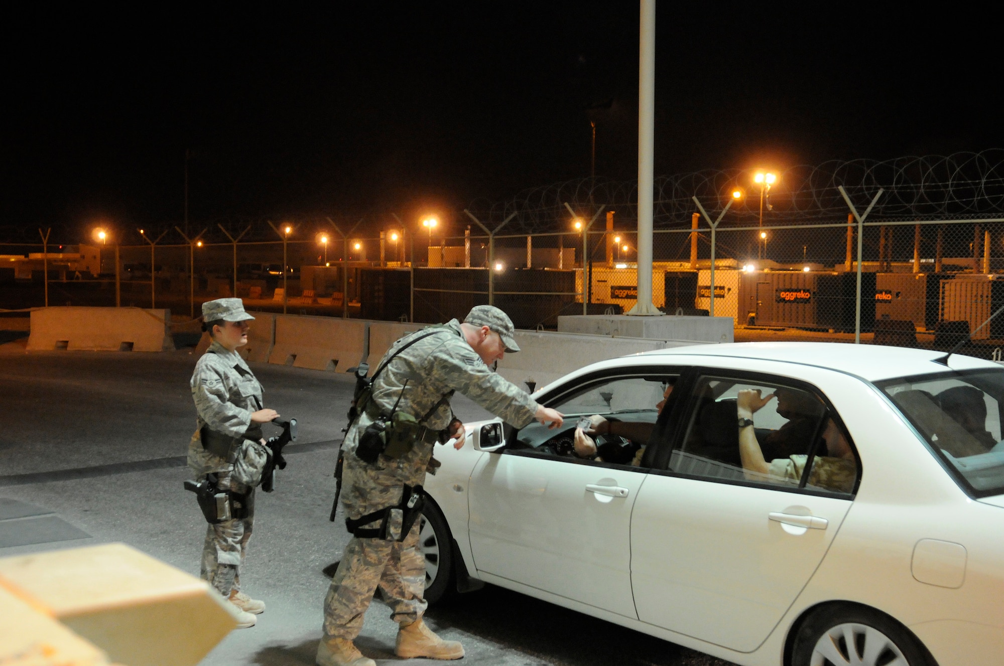 Senior Airman William Baker, 379th Expeditionary Security Forces Squadron, examines a driver's identification prior to allowing the vehicle through a checkpoint, Nov. 21, at an undisclosed air base in Southwest Asia.  Airman 1st Class Kari Kasprzyk, 379 ESFS, provides security back-up from a distance.  Air Force Security Forces members write and implement resource protection, policing and security activities for joint and coalition partners at this Central Command air base.  Airman Baker hails from Frankfurt, Germany, and is deployed from Spangdahlem Air Base, Germany.  Airman Kasprzyk is a native of Enumclaw, Wash., and is deployed from Hill Air Force Base, Utah.  Both Airmen are deployed in support of Operations Iraqi and Enduring Freedom and Joint Task Force-Horn of Africa.  (U.S. Air Force photo by Tech. Sgt. Michael Boquette/Released)