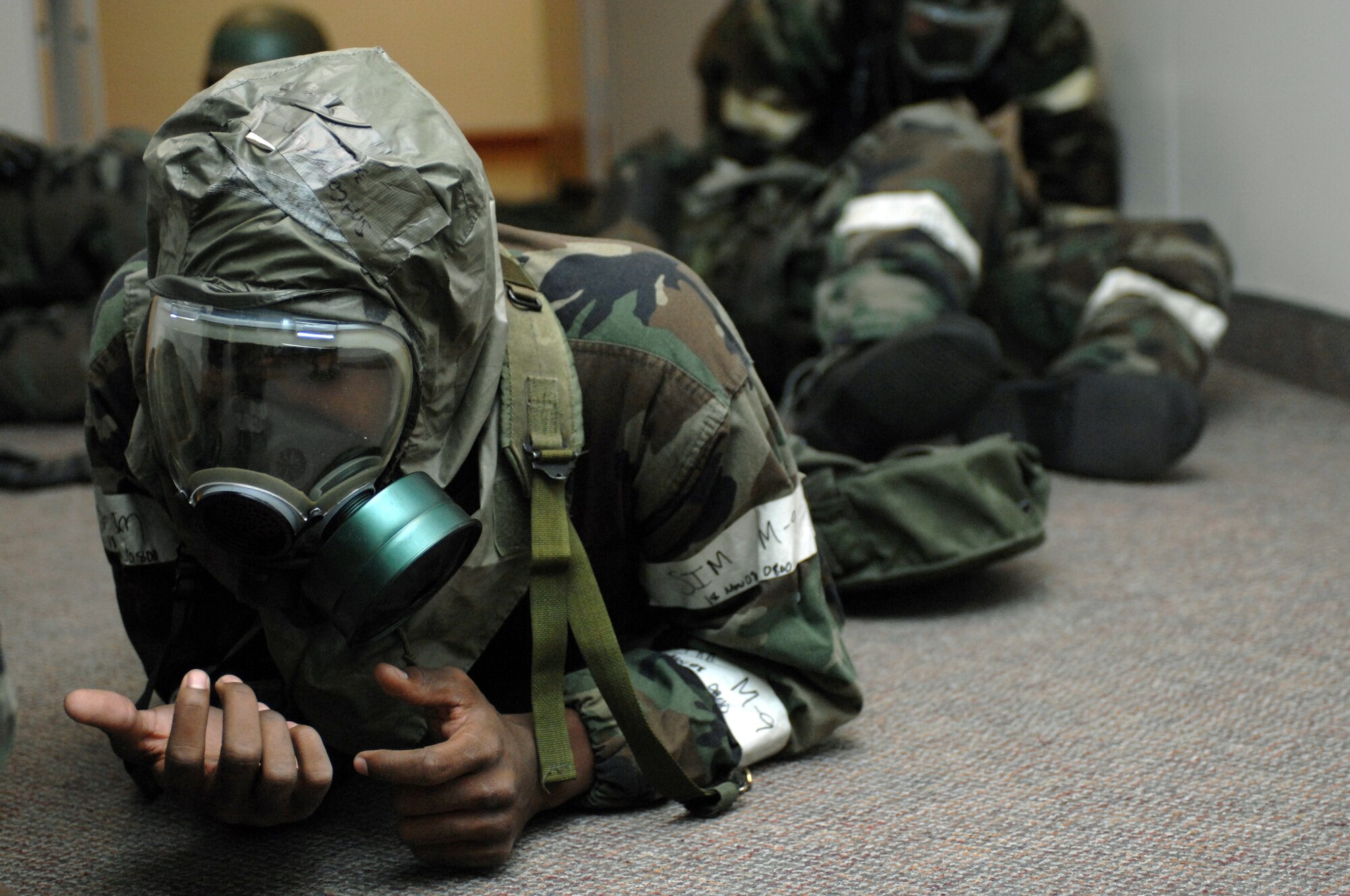 Senior Airman Sean Cooper, 49th Force Support Squadron, simulates chemical burns on his hands while crawling out of a room in the Military Personnel Flight (MPF) building during a phase II exercise at Holloman Air Force Base, N.M., Nov. 19. The scenario was that a room in the MPF building exploded while the base was under attack. Many Airmen had to perform self-aid and buddy care while in mission oriented protective posture (MOPP) 4, which included a chemical suit, boots, gloves and a gas mask. (U.S. Air Force photo/Airman Sondra M. Escutia)