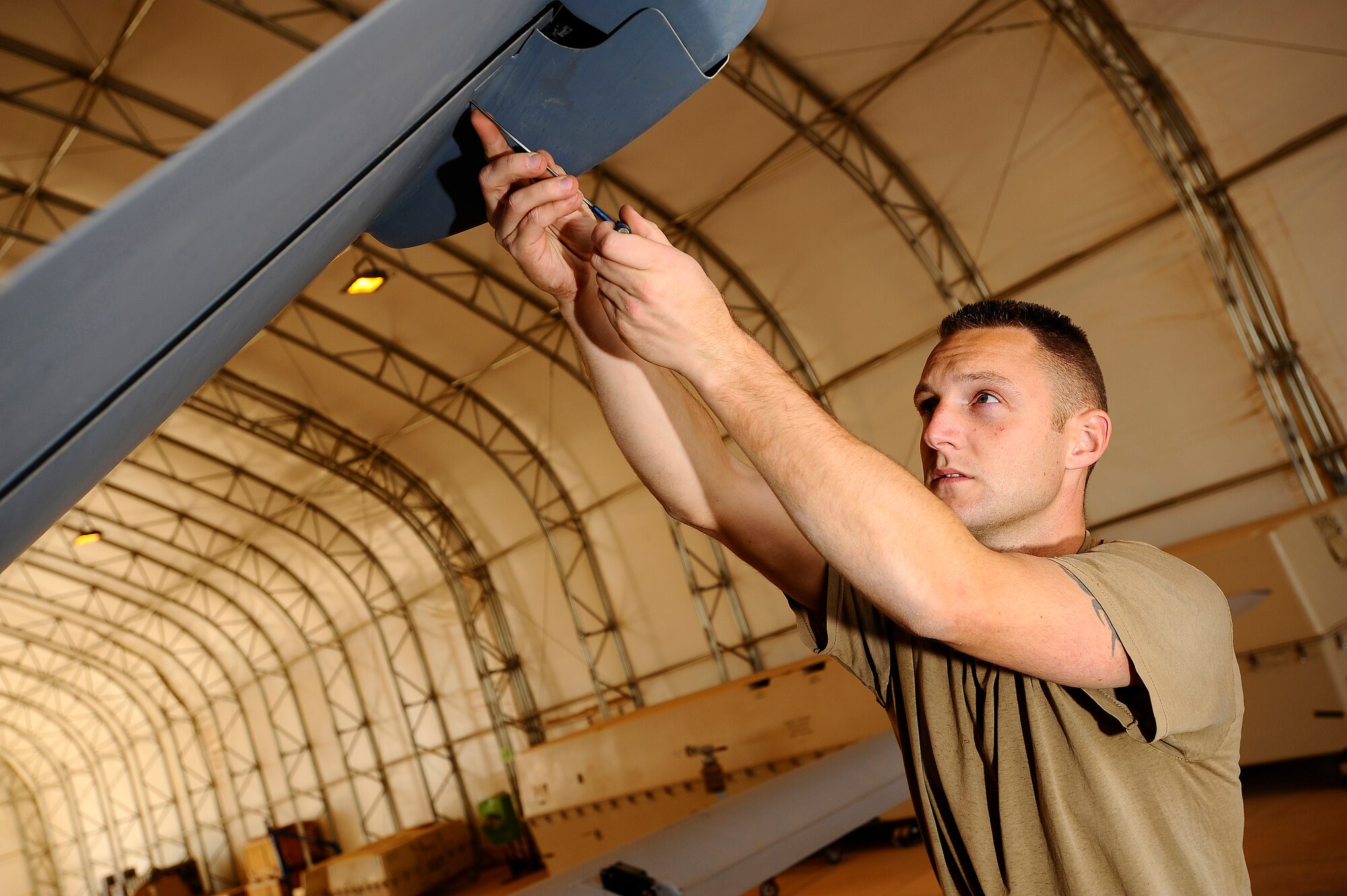 Royal Air Force Corporal Jon Watt attaches a servo actuator cover to the diagonal tail of an MQ-9 Reaper at Joint Base Balad, Iraq, Nov. 22. A coalition force of experts from the U.S. Air Force and Royal Air Force deployed here to man a new Reaper aircraft maintenance unit. The unit is attached to the 46th Expeditionary Reconnaissance and Attack Squadron and assumed maintenance duties from General Atomics, which produces the Reaper for these services. Watt, a Reaper avionics specialist assigned to the 332nd Expeditionary Aircraft Maintenance Squadron, is deployed from Creech Air Force Base, Nev. His hometown is Plymouth, England. (U.S. Air Force photo/Airman 1st Class Jason Epley)(Released)