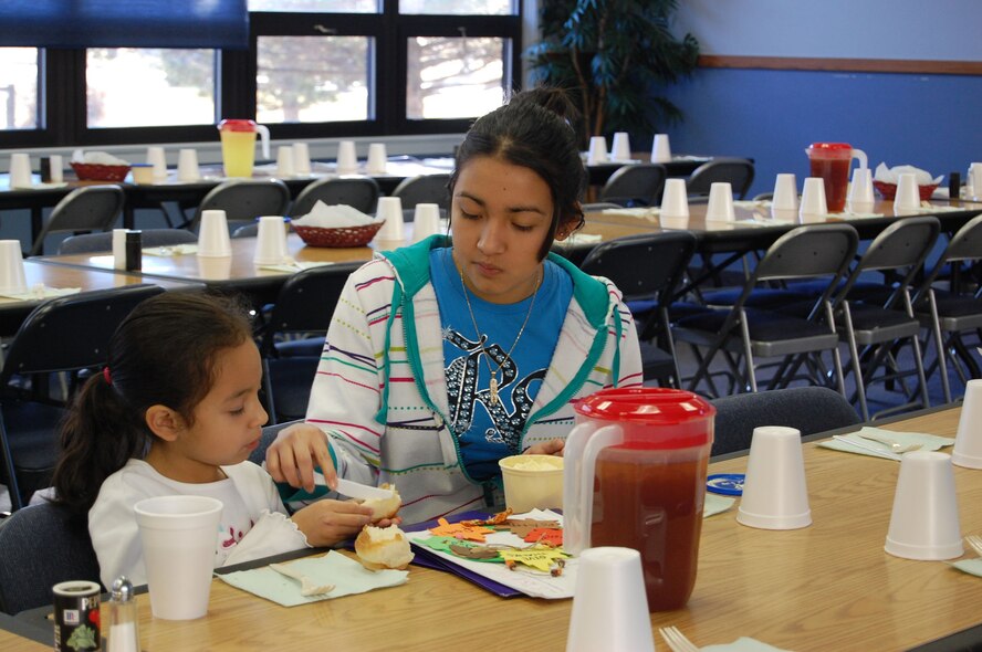 Nicole Garcia, 14, butters a dinner roll for her sister, Jiselle, 5, before the start of the chapel's annual community dinner Nov. 23. Nicole and other members of the chapel youth group helped get the tables ready. (U.S. Air Force photo/Valerie Mullett)