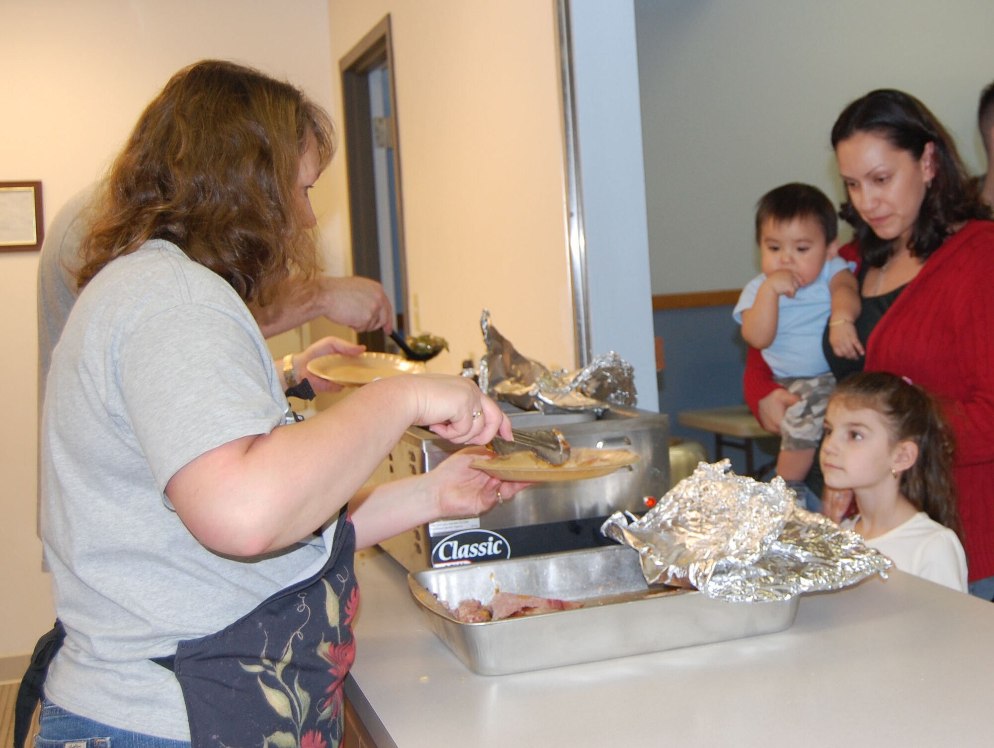 Five-year-old Xani watches as chapel caterer Trina Jackson serves up her food at the chapel's annual community dinner Nov. 23. Her mom, Michele, and 9-month-old brother Pheonix, wait to get their food next. (U.S. Air Force photo/Valerie Mullett)