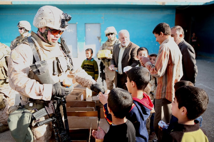 Cpl. Drew March, a fire team leader, Provisional Rifle Platoon 3, Regimental Combat Team 5, hands out treats to elementary school children in Rawah, Iraq, Nov. 25. The school children were surprised by the gifts, a surplus of snacks the Marines wanted to share with the neighborhood.::r::::n::