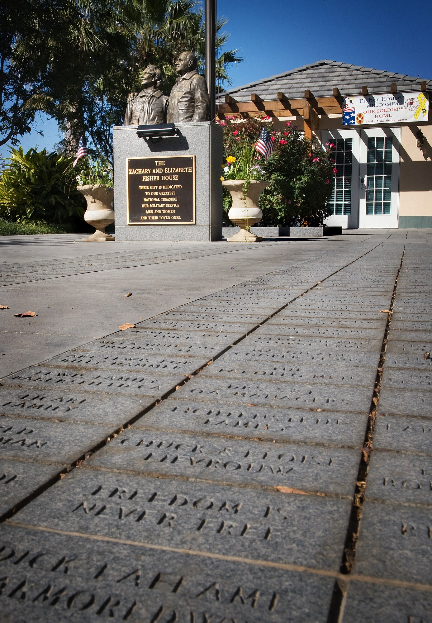 Names of generous donors etched into paver stones surround a statute dedicated to Zachary and Elizabeth Fisher in a courtyard between the two newer Fisher Houses in San Antonio on Nov. 25.  Each of these 16,800 square foot Fisher Houses can accommodate up to 42 families visiting their injured love ones. Private donations were used to fund their construction, operation and maintenance. (U.S. Air Force photo/Lance Cheung)