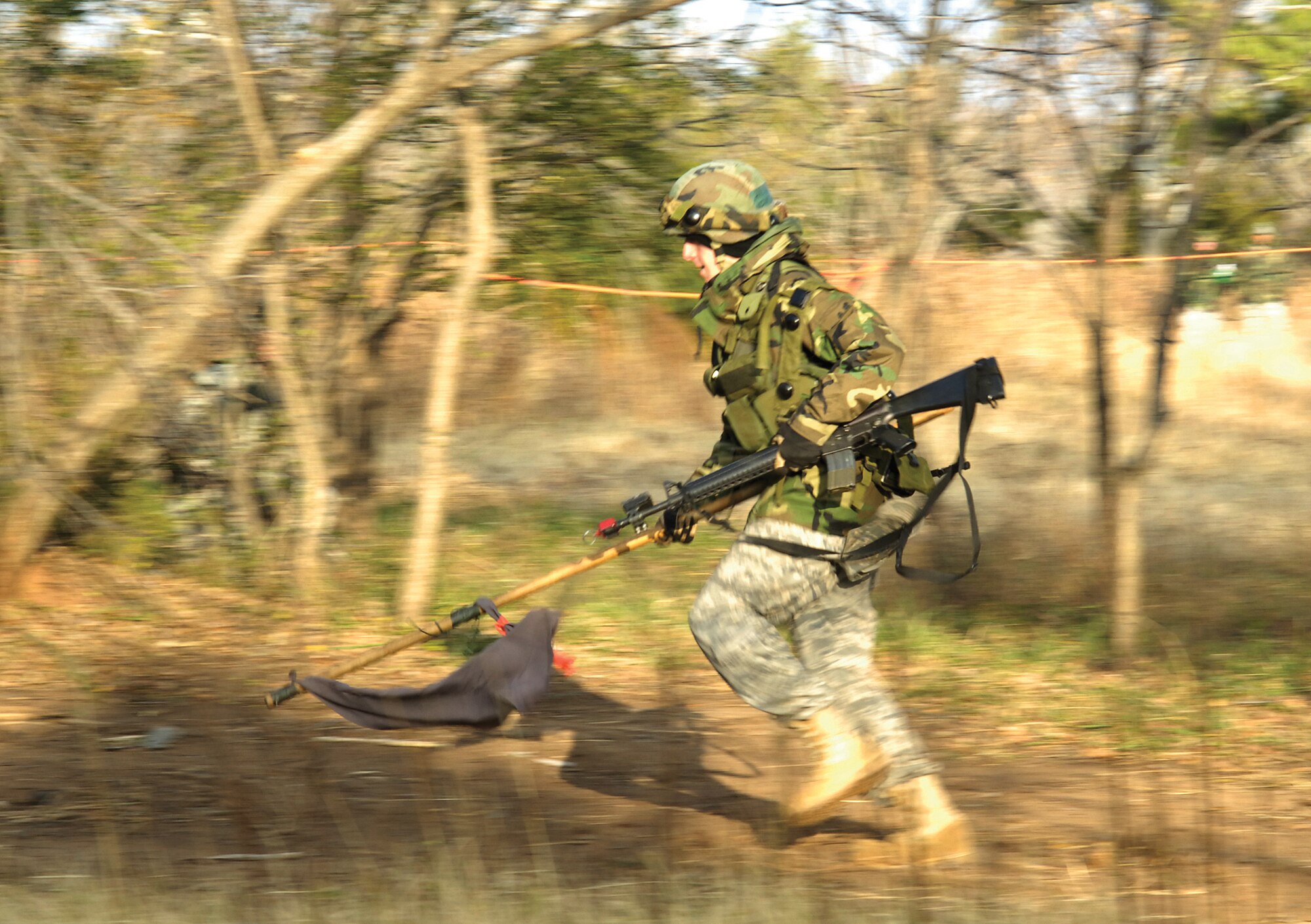 The sound of weapons fire surrounds a 3rd Combat Communications Group Airman who races to friendly ground with a flag captured during a Hooahlympics event.  Lasers and blank ammo, MILES gear, was used to test accurateness under pressure during the annual combat-styled competitions held Nov. 20 at the Glenwood Training Area.  Squadrons gave their best in tests of self-aid buddy care, land navigation, tire changing, running and weapons disassembly/assembly.  (Air Force photo/Margo Wright)