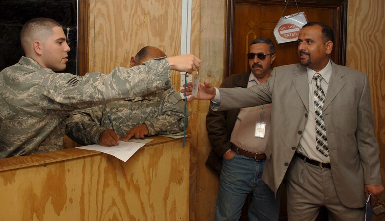 Senior Airman Anthony Camacho, 332nd Expeditionary Security Forces Group, hands a visitor badge to a local Iraqi visiting the Iraqi-Based Industrial Zone area outside an entry control point at Joint Base Balad, Iraq, Nov. 20. U.S. servicemembers contracted a project, which included a new waiting room and security fence upgrade, at the ECP to enhance relations with the Iraqis who visit here to work, conduct business or seek medical assistance. Camacho is a San Antonio native deployed from Lackland Air Force Base, Texas. (U.S. Air Force photo/Tech. Sgt. Erik Gudmundson)