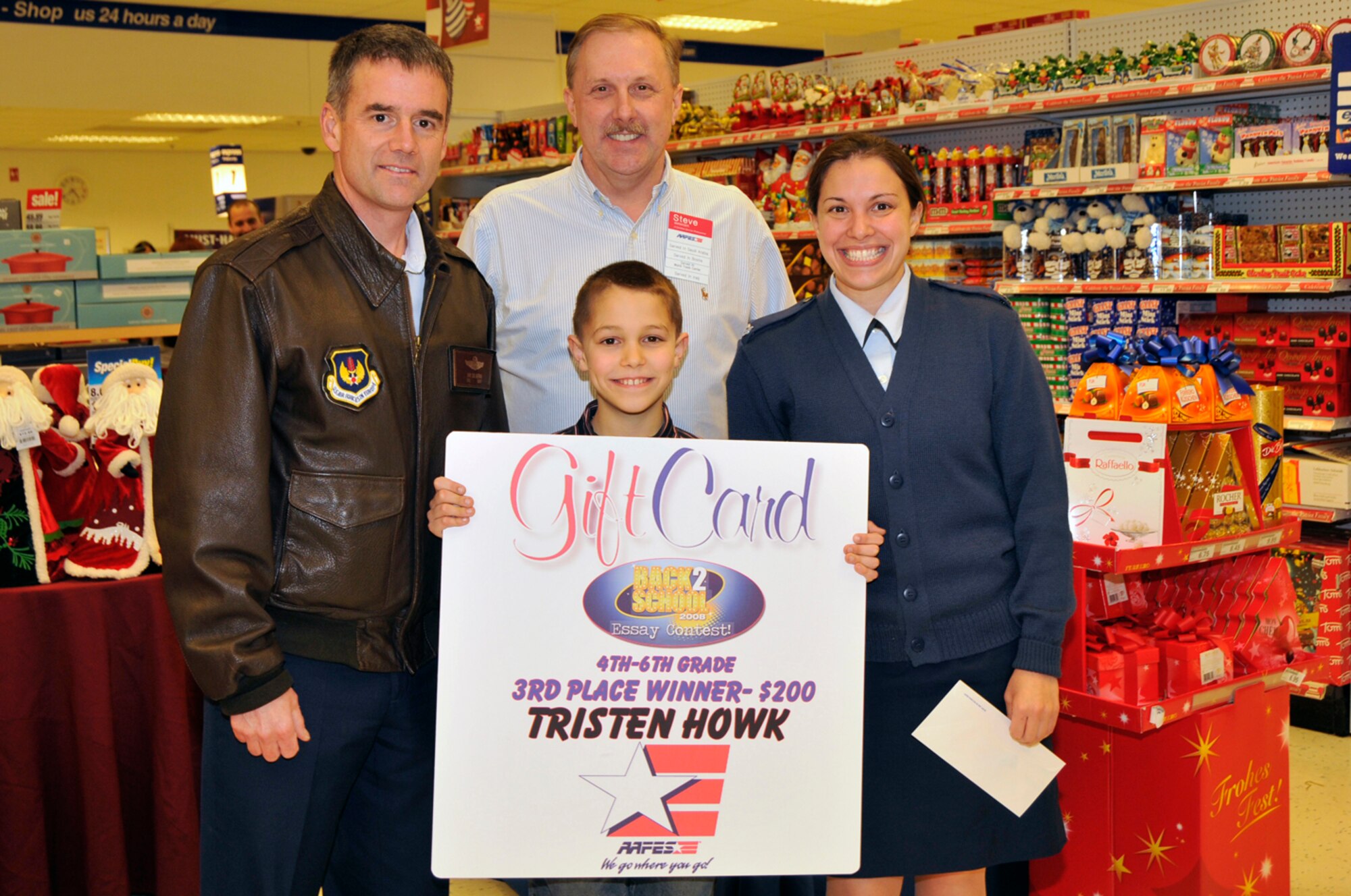 Tristen Howk, third place winner of the AAFES Back to School Essay Contest poses with Colonel Jay B. Silveria, 48th Fighter Wing Commander, Steve Williams, AAFES General Manager, and his mother Staff Sgt. Theresa Newell Nov. 24 at RAF Lakenheath, England. Students in grades first through twelfth had the opportunity to submit an essay of 200 words or less on “What AAFES means to me and my family." (U.S. Air Force photo by Airman 1st Class Perry Aston) 