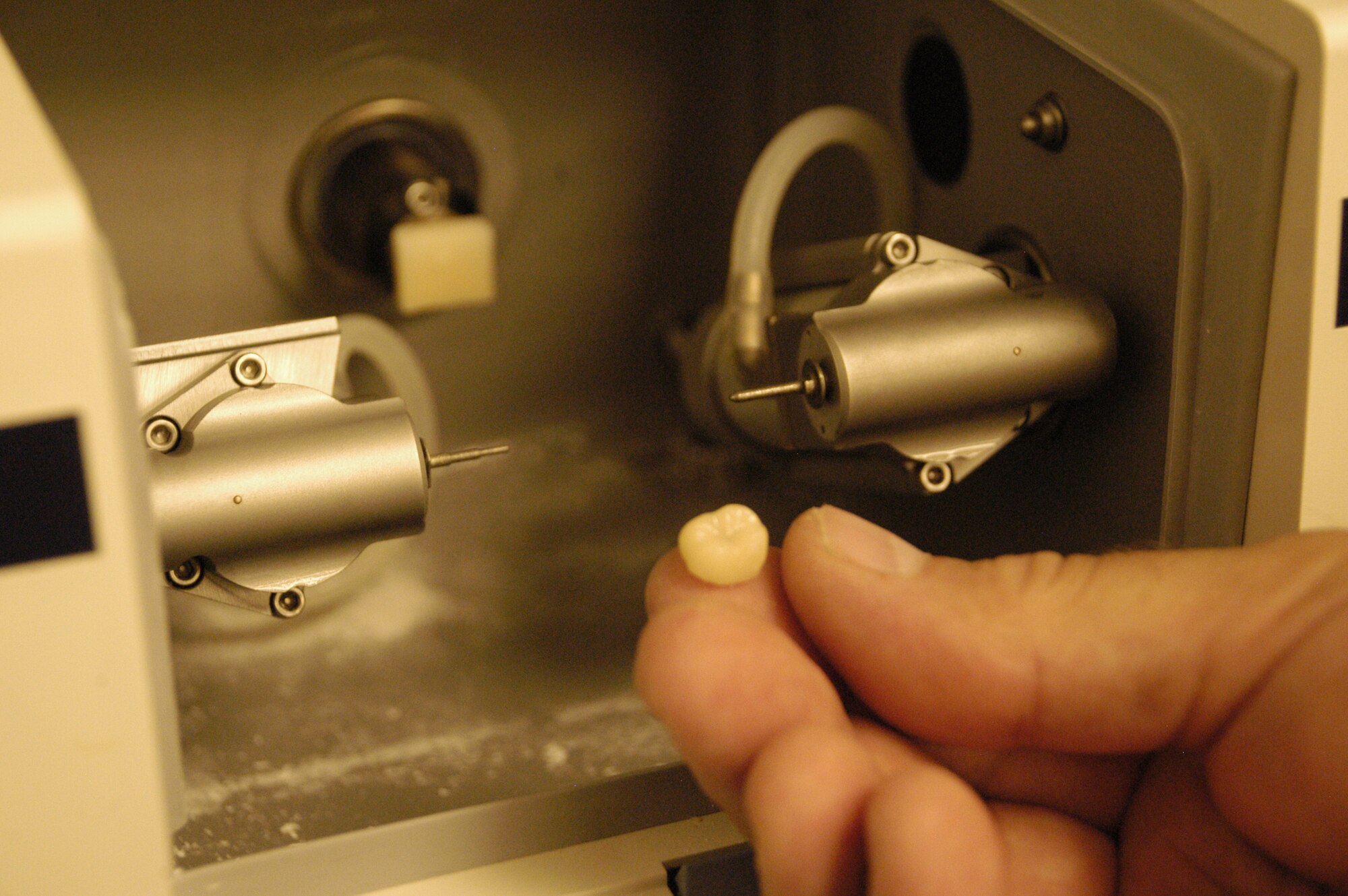 DOVER AIR FORCE BASE, Del. – Tech. Sgt. Raymond Worl, 436th Dental Squadron NCO in-charge of the dental laboratory, holds a finished crown tooth. The dentist takes a picture of a patient’s tooth and the information is transferred to a milling instrument. A porcelain block is placed inside the milling unit and the machine automatically molds the porcelain block with metal burs to create the finished product. The Computer Aid Design machine allows dental lab technicians to eliminate several steps in tooth fabrication which cuts down the time needed to make a crown without using metal. (U.S. Air Force photo/ Airman 1st Class Shen-Chia Chu)