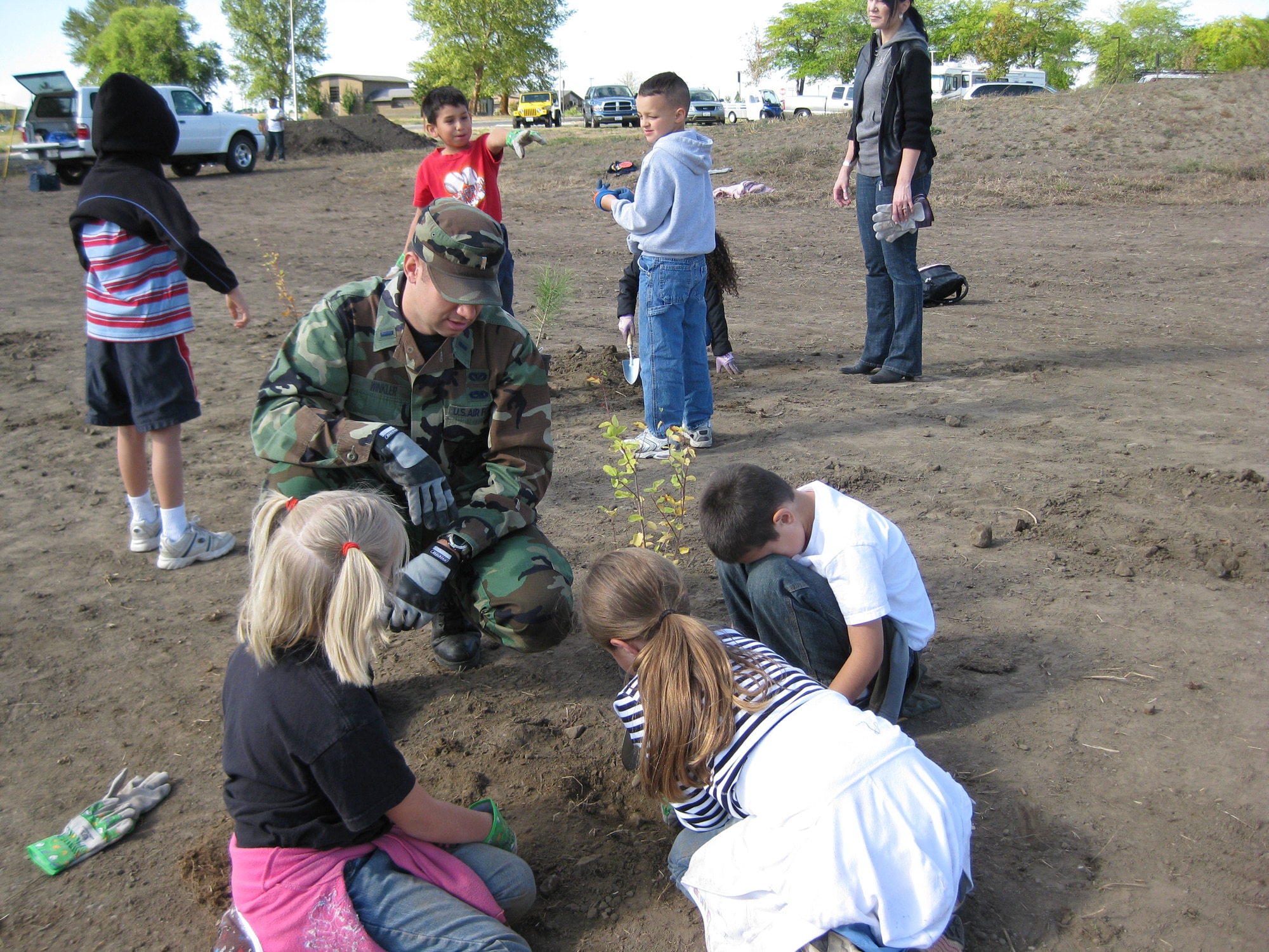 First Lt. Hans Winkler, 92nd Civil Engineer Squadron, helps kids from Michael Anderson Elementary plant a native shrub (common snowberry) on National Public Lands Day celebrated Sept. 25 at Fairchild. (U.S. Air Force photo / Mary Farver)