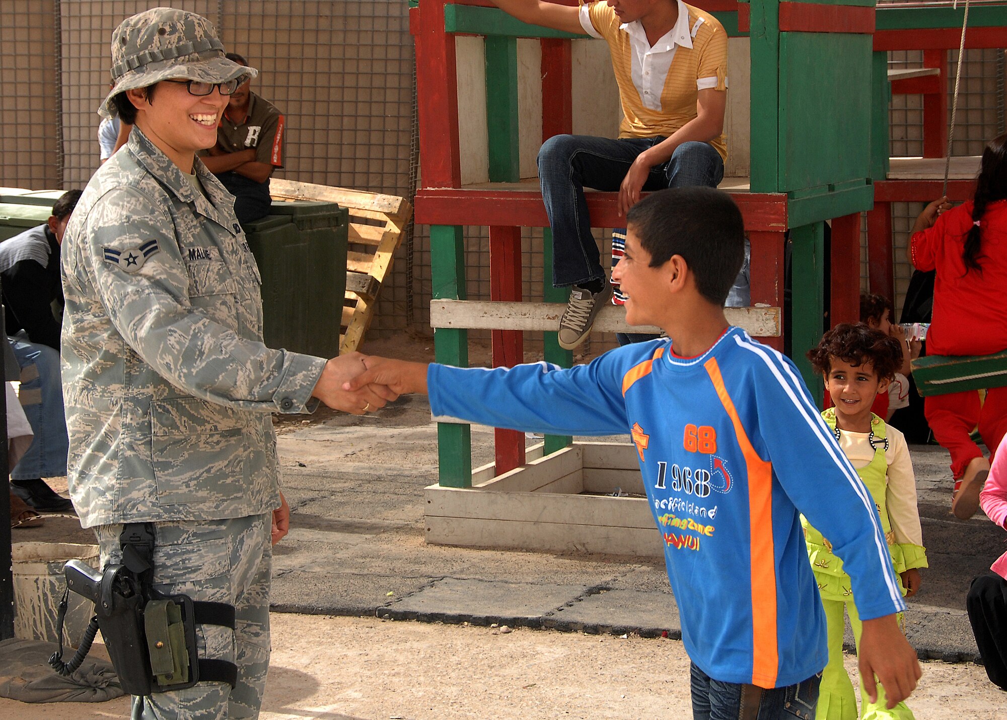 Camp Bucca, Iraq -- Airman 1st Class Martina Malone, a Security Forces member assigned to the 887th Expeditionary Security Forces Squadron, receives a handshake from an Iraqi boy waiting to visit his father at the Theater Internment Facility (TIF) at Camp Bucca, Iraq, on Sept. 29. The 887th ESFS controls access to detainees  at the TIF and processes visitation procedures for family members. The Air Force works side by side with Army Soldiers in manning the facility, which houses more than 18,000 detainees. Airman Malone is deployed from Dyess Air Force Base, Texas. (U.S. Air Force photo/Tech. Sgt. Raheem Moore)