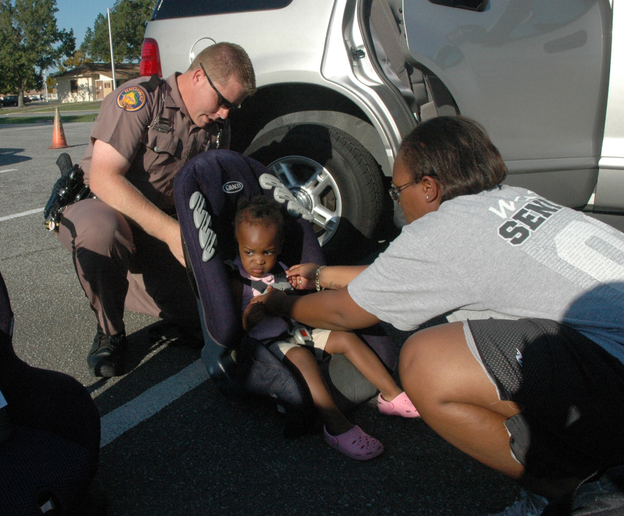 Florida Trooper James Swearingin demonstrates to Staff Sgt. Shirae Hines, 325th Fighter Wing Legal Office client support administrator, how to properly strap and adjust her daughter, Macayla, into a car seat during Tyndall’s car seat check Sept. 25. (U.S. Air Force photo by Airman 1st Class Veronica McMahon)
