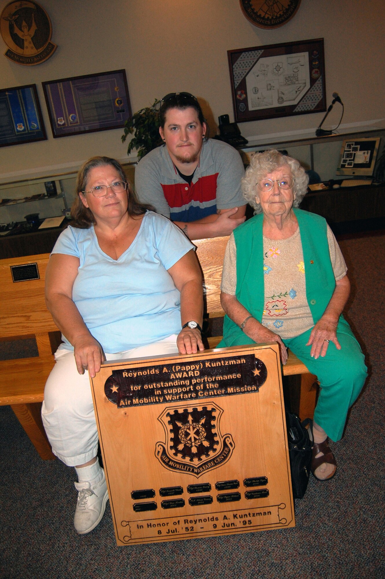 Valerie (spouse), Jeremy (son), and Helen Kuntzman (mother) stop for a photo by the plaque bearing the name of former Tech. Sgt. Reynolds A. Kuntzman, during a visit to the U.S. Air Force Expeditionary Center Aug. 21, 2008.  Sergeant Kuntzman died on June 9, 1995, while assigned to the center with the 421st Ground Combat Readiness Squadron.  After his death, the center's leadership created the Reynolds A. Kuntzman Duty performance award given annually to an Airman in the grades of E-1 through E-6 recognizing superior duty performance in support of the center's mission and community.  (U.S. Air Force Photo/Tech. Sgt. Scott T. Sturkol)