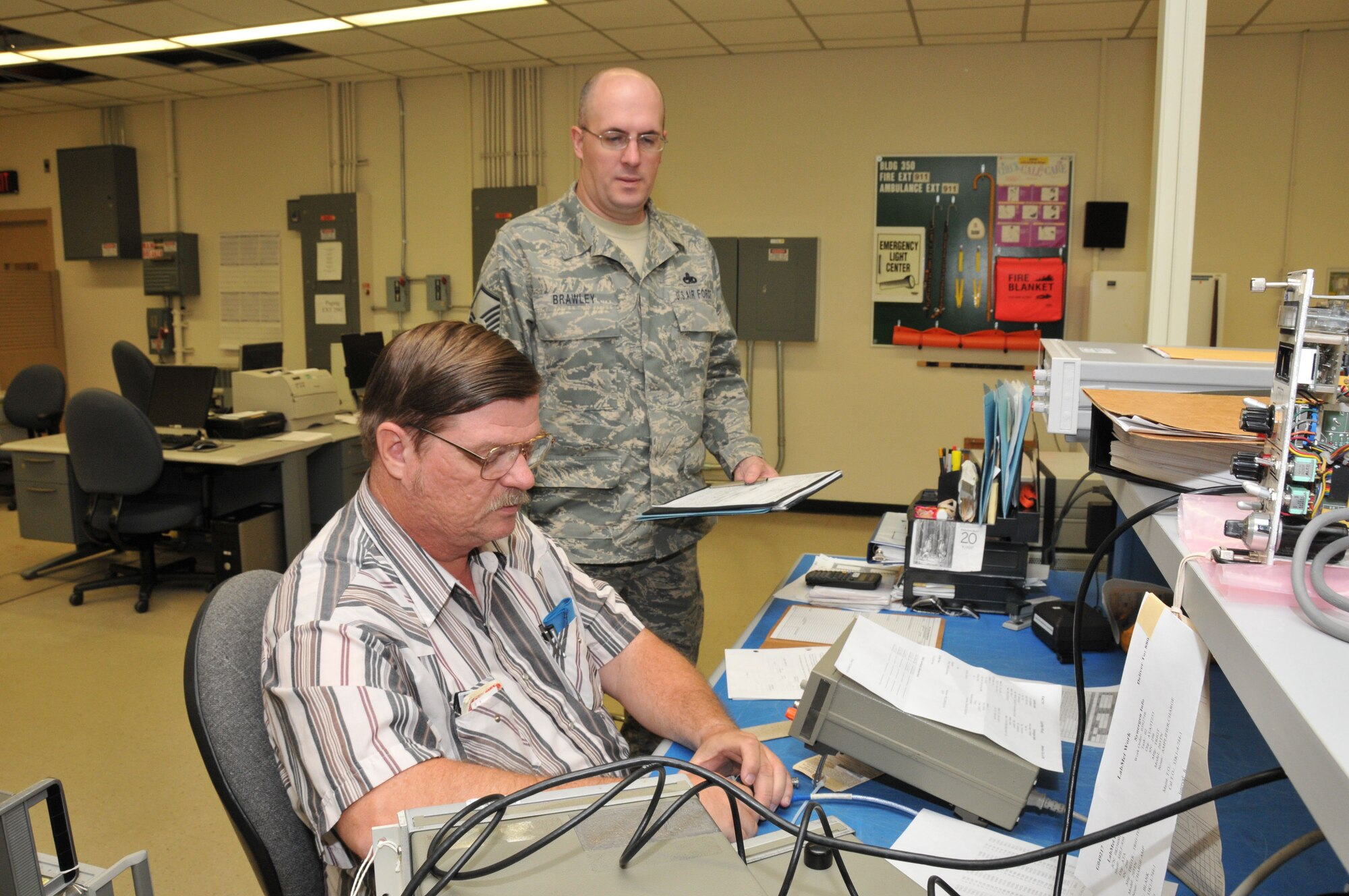 Master Sgt. Clinton Brawley, the Precision Measurement Equipment Laboratory (PMEL) QA Section Chief at Holloman Air Force Base, N.M., conducts an over-the-shoulder inspection of a frequency counter calibration with Arnold Engineering Development Center’s Hal Corum, PMEL instrument technician. (Photo by David Housch) 

