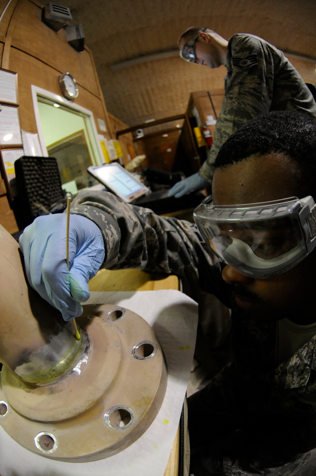 Senior Airman Tysean Wilson, 379th Expeditionary Maintenance Squadron non-destructive inspection journeyman, cleans a part prior to inspection while Staff Sgt. Craig Hadrych, non-destructive inspection craftsman enters data into a computer at a Southwest Asia base Sept. 25. Airman Wilson, a native of Yuba City, Calif., is deployed from Langley Air Force Base, Va., and Sergeant Hadrych, a native of Eden, N.Y., is deployed from RAF Mildenhall, United Kingdom. (U.S. Air Force photo by Darnell Cannady)
