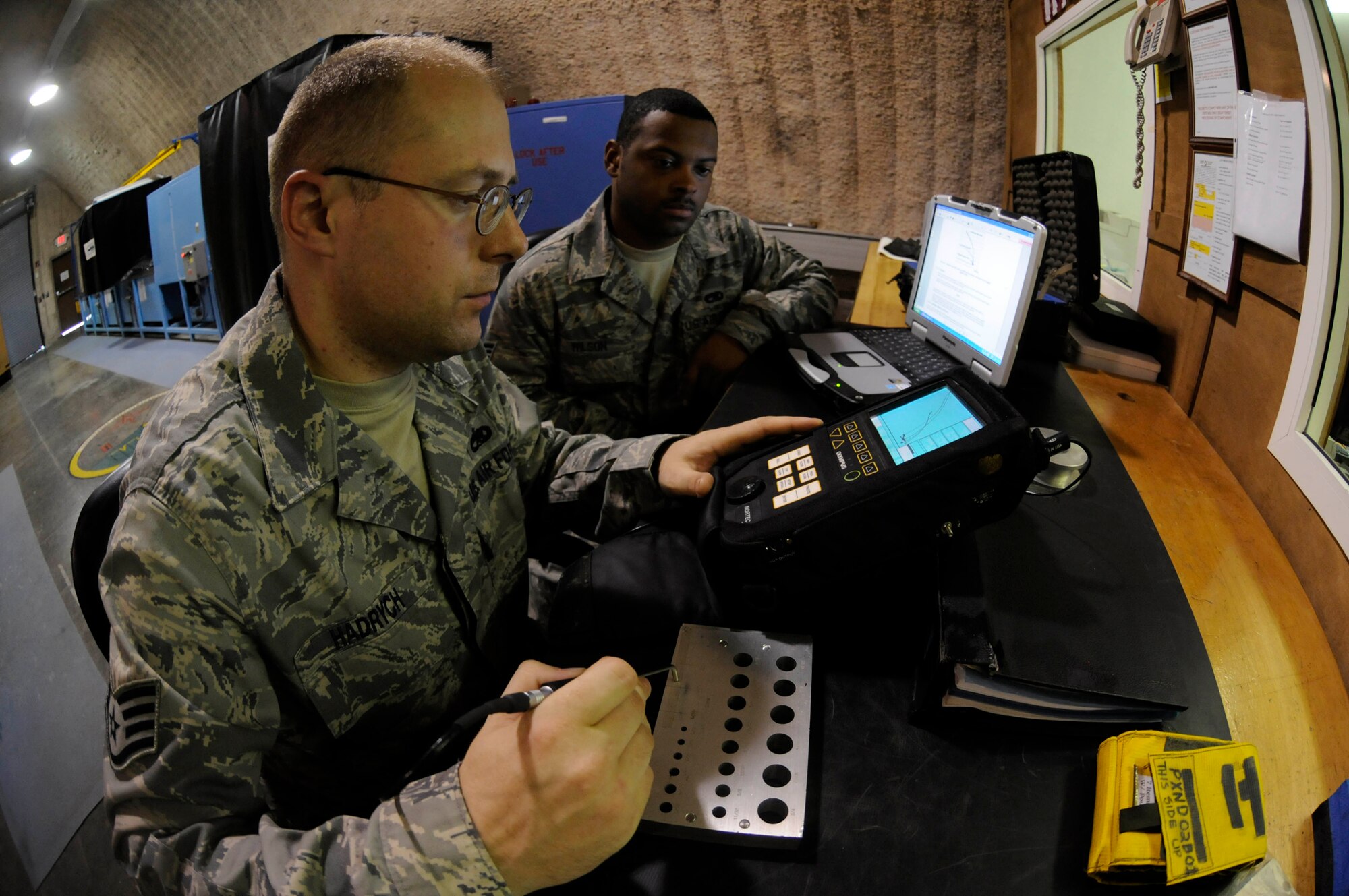 Staff Sgt. Craig Hadrych, 379th Expeditionary Maintenance Squadron non-destructive inspection craftsman, calibrates the Nortec 2,000 eddy current flaw detection instrument using a reference standard while Senior Airman Tysean Wilson, non-destructive inspection journeyman, reviews the technical orders on a laptop at a Southwest Asia base Sept. 25. Airman Wilson, a native of Yuba City, Calif., is deployed from Langley Air Force Base, Va., and Sergeant Hadrych, a native of Eden, N.Y., is deployed from RAF Mildenhall, United Kingdom.(U.S. Air Force photo by Staff Sgt. Darnell T. Cannady)