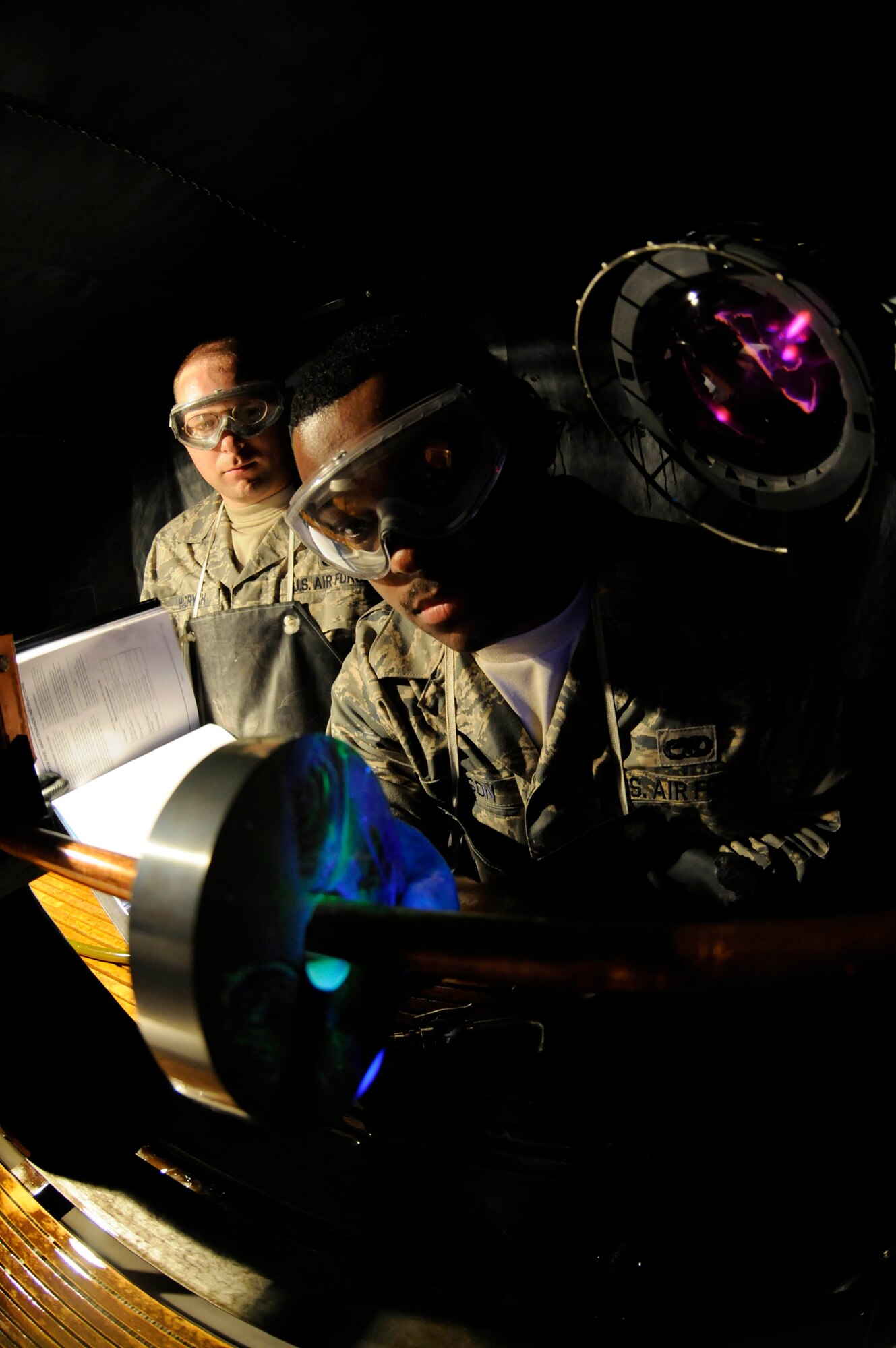 Senior Airman Tysean Wilson, non-destructive inspection journeyman assigned to the 379th Expeditionary Maintenance Squadron, performs a system effectiveness check by using a black light to look for subsurface defects on a ketos ring while Staff Sgt. Craig Hadrych, non-destructive inspection craftsman, reviews the technical orders at a Southwest Asia base Sept. 25, 2008. Non-destructive inspection Airmen are responsible for ensuring there are no cracks or defects in maintenance materials issued here. Airman Wilson, a native of Yuba City, Calif., is deployed from Langley Air Force Base, Va., and Sergeant Hadrych, a native of Eden, N.Y., is deployed from RAF Mildenhall, United Kingdom. (U.S. Air Force photo by Staff Sgt. Darnell T. Cannady)