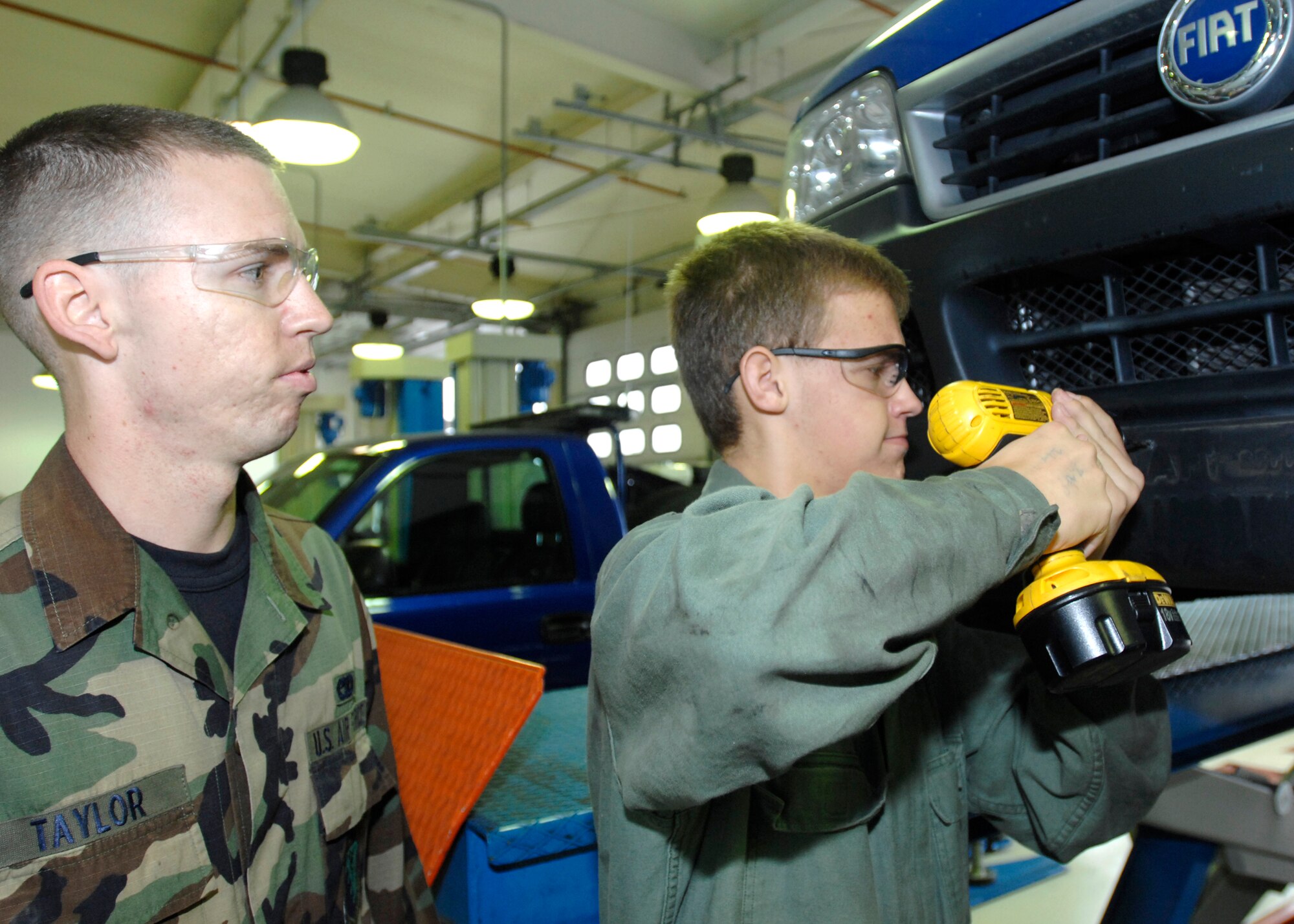 Airman 1st Class Bryan Taylor of the 31st Logistics Readiness Squadron oversees Aviano High School senior Austin Cooper as he uses a power tool to work on a car at vehicle maintenance shop. Tyler is interning with the 31st LRS as part of the Aviano High School career practicum course, which affords students the opportunity to intern with base units that feature the student's career field of interest. (U.S. Air Force photo/Airman 1st Class Ashley Wood)